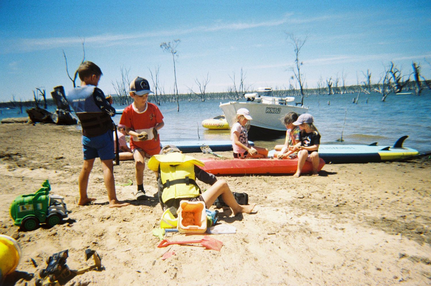 Beach scene with kayaks and beach toys scattered on the sandy shore.