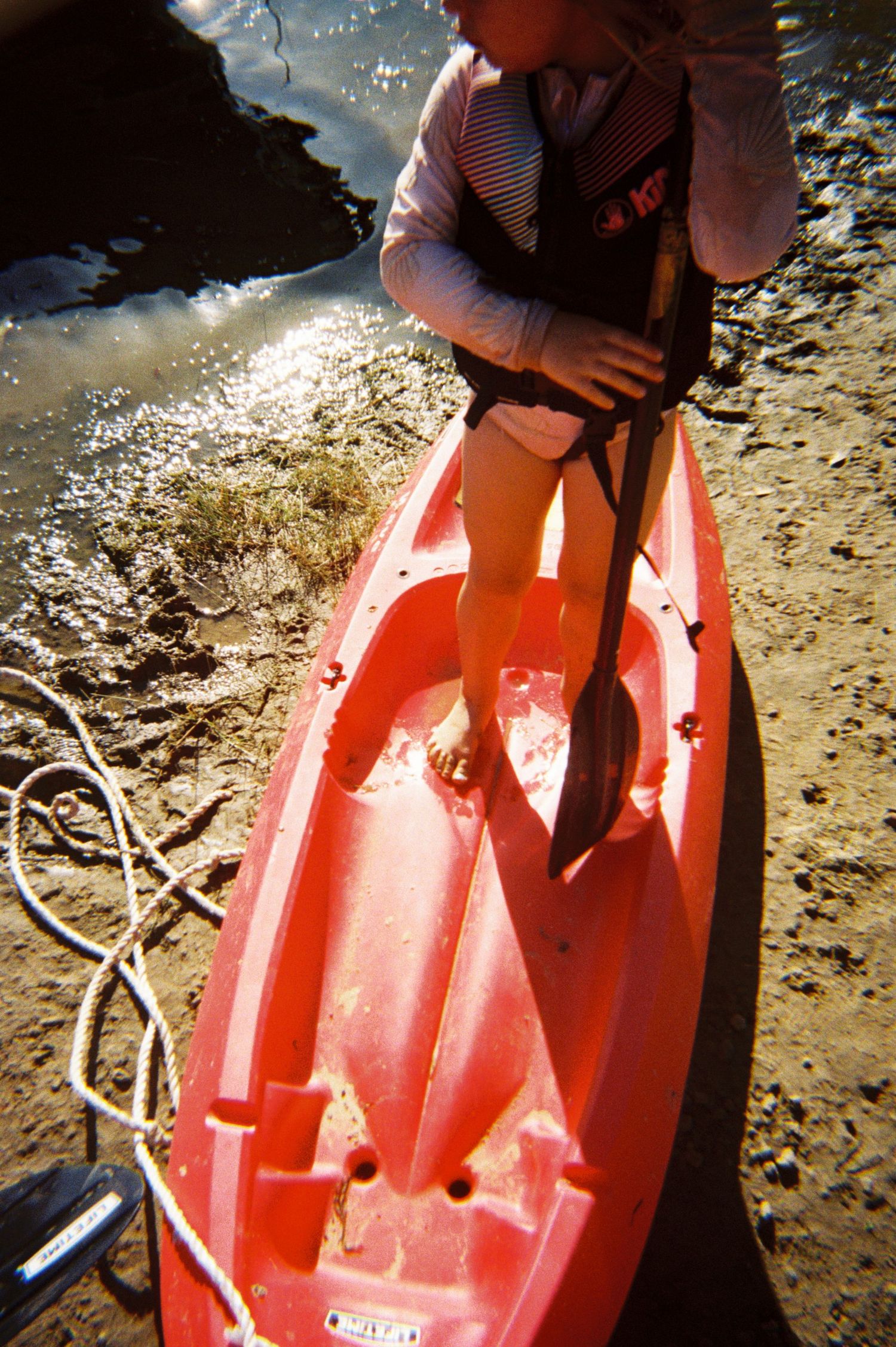 Close-up of a red kayak on the beach shore with sunlit water in background.