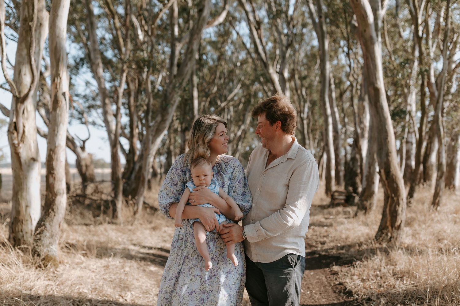 A couple embraces in a sunlit eucalyptus grove during an outdoor photoshoot.