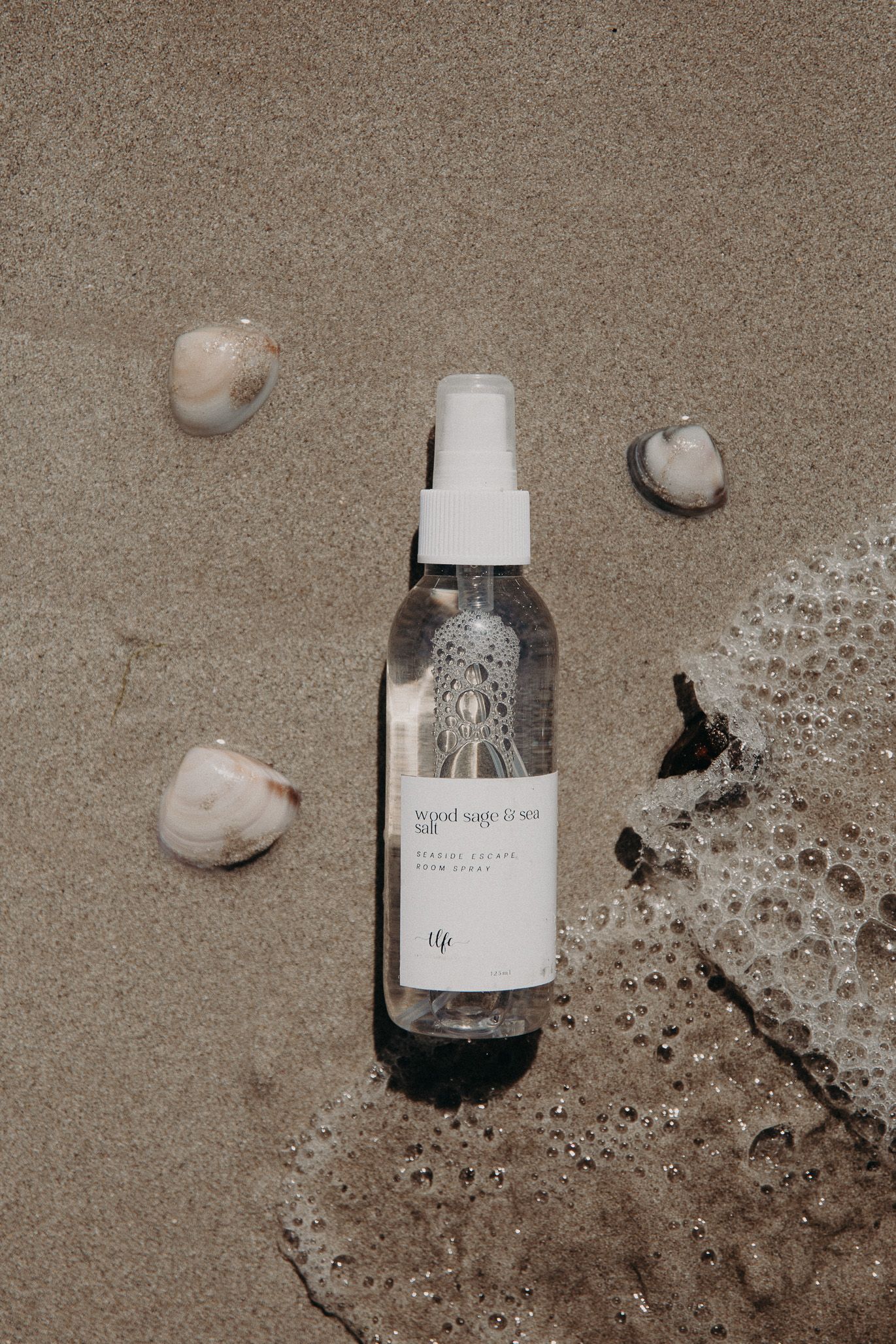 Clear spray bottle on sandy beach with seashells.