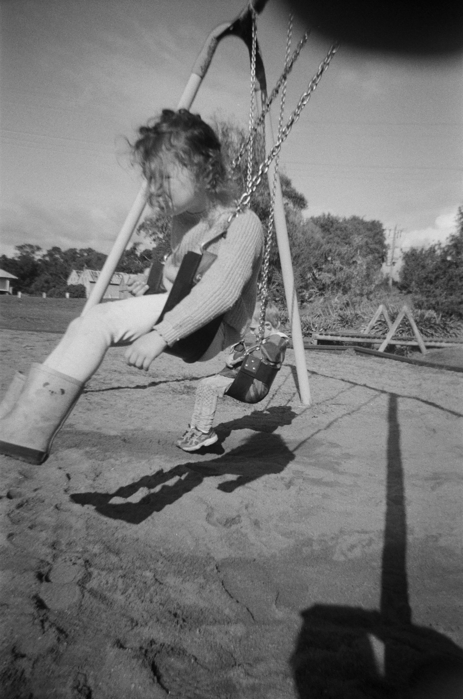 Black and white sequence showing someone swinging on a playground swing set casting long shadows.