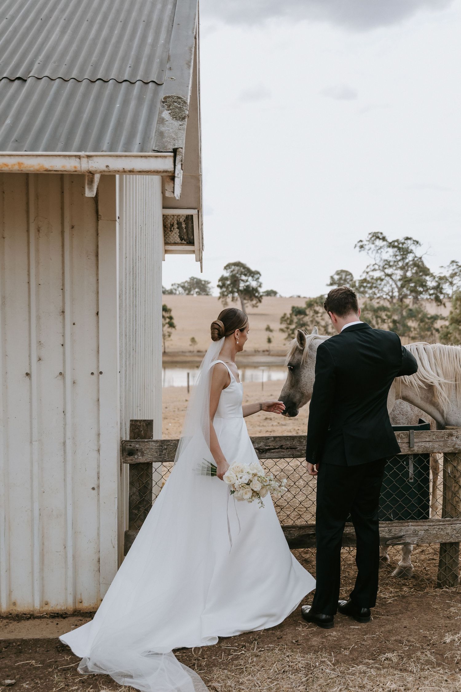 Wedding couple in formal attire walking outside a rustic white building.