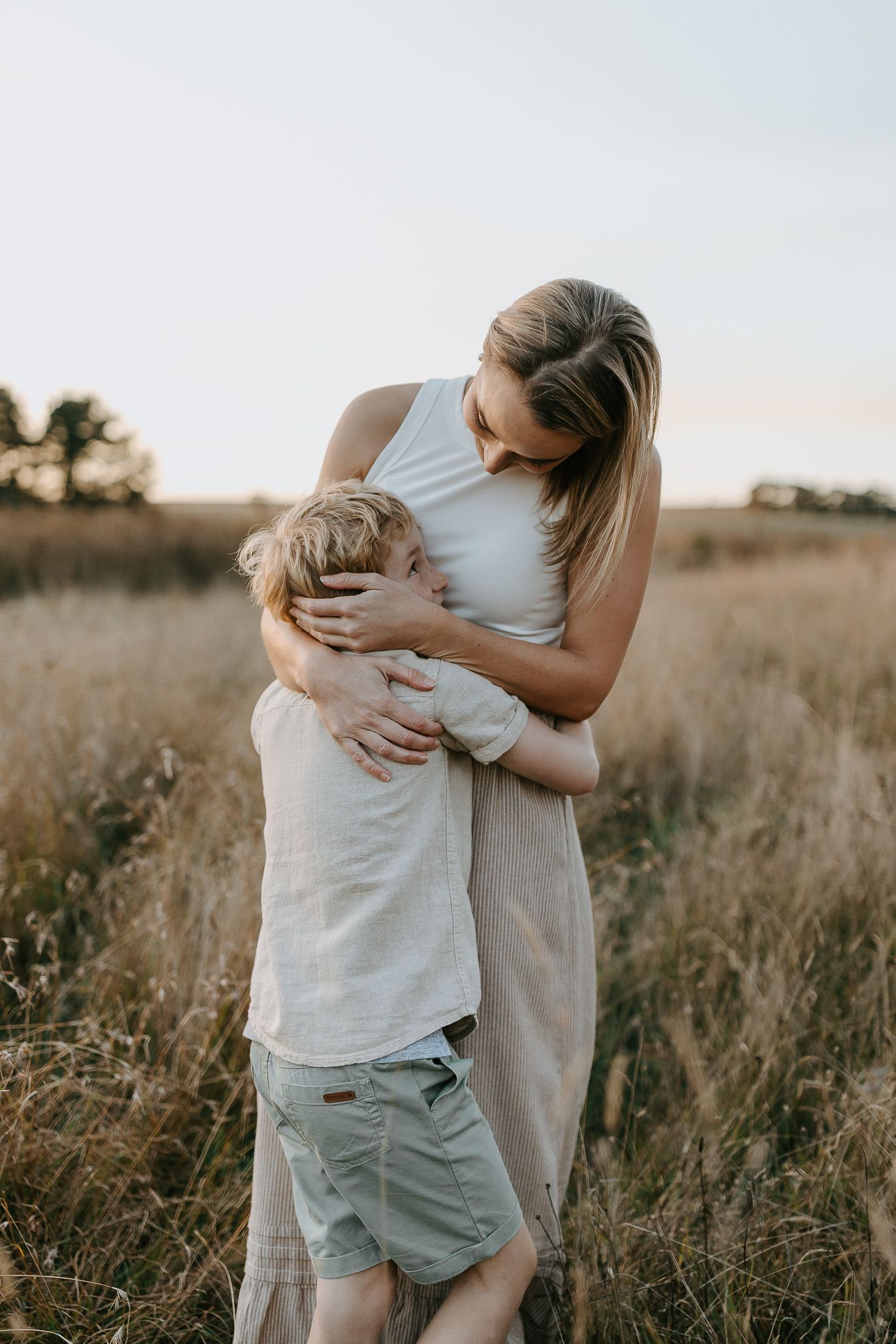 Tender moment between parent and child embracing in a golden field at sunset.