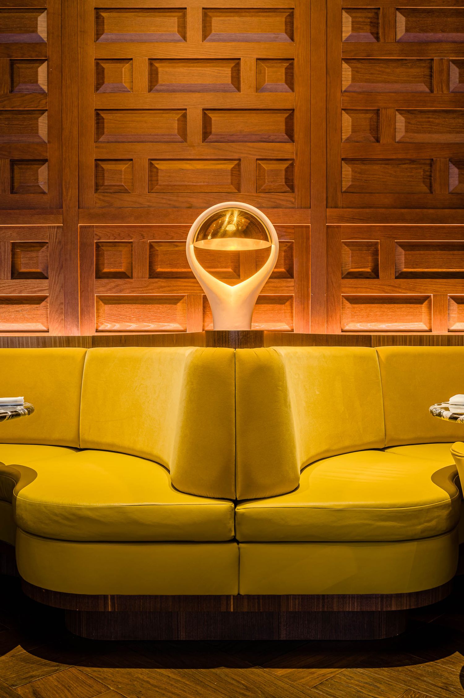Detalle de interiorismo: sofá curvo amarillo y panelado de roble en el hotel The Madrid Edition. Estética de lujo y autor