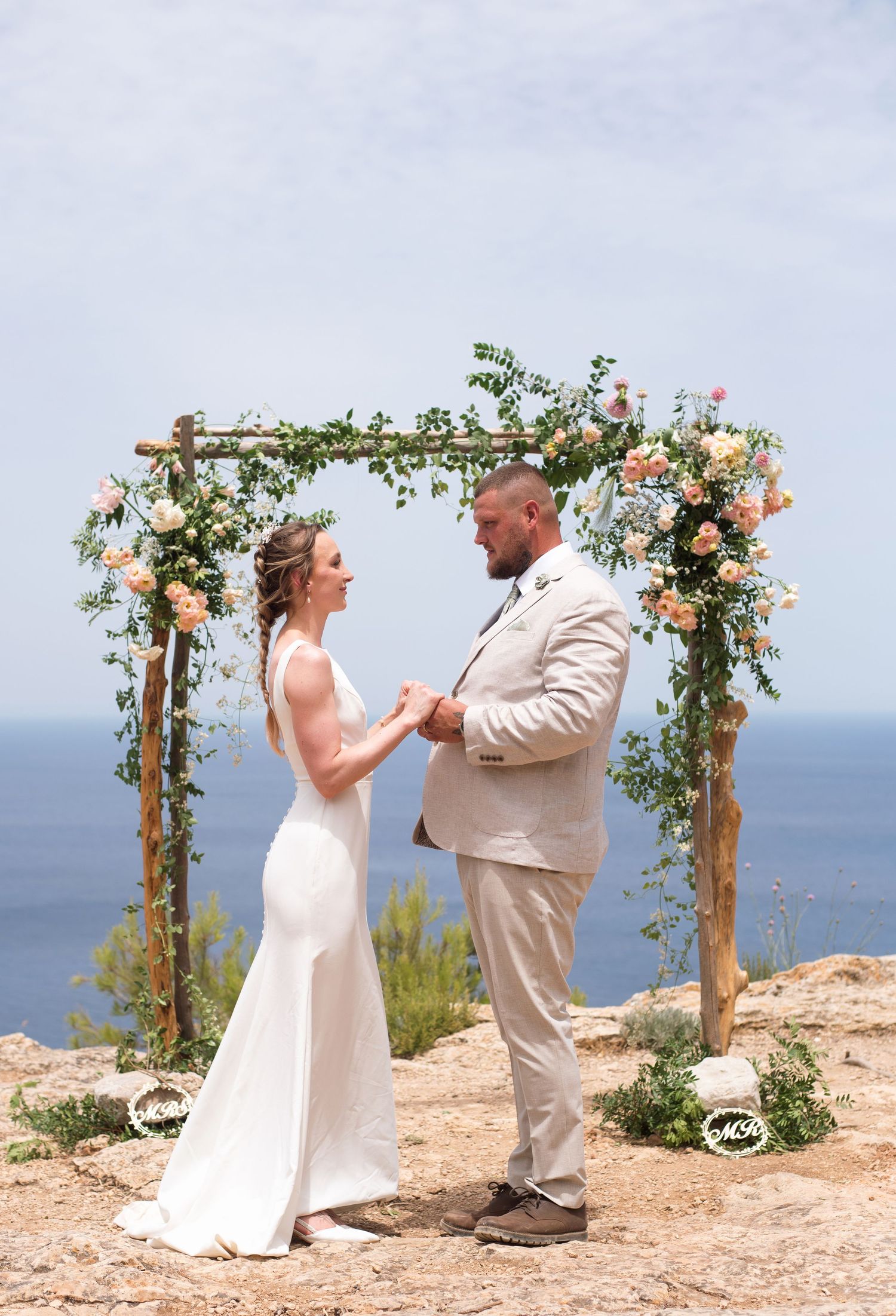 Couple exchanging vows under a floral arch with ocean views at a cliffside outdoor wedding ceremony.