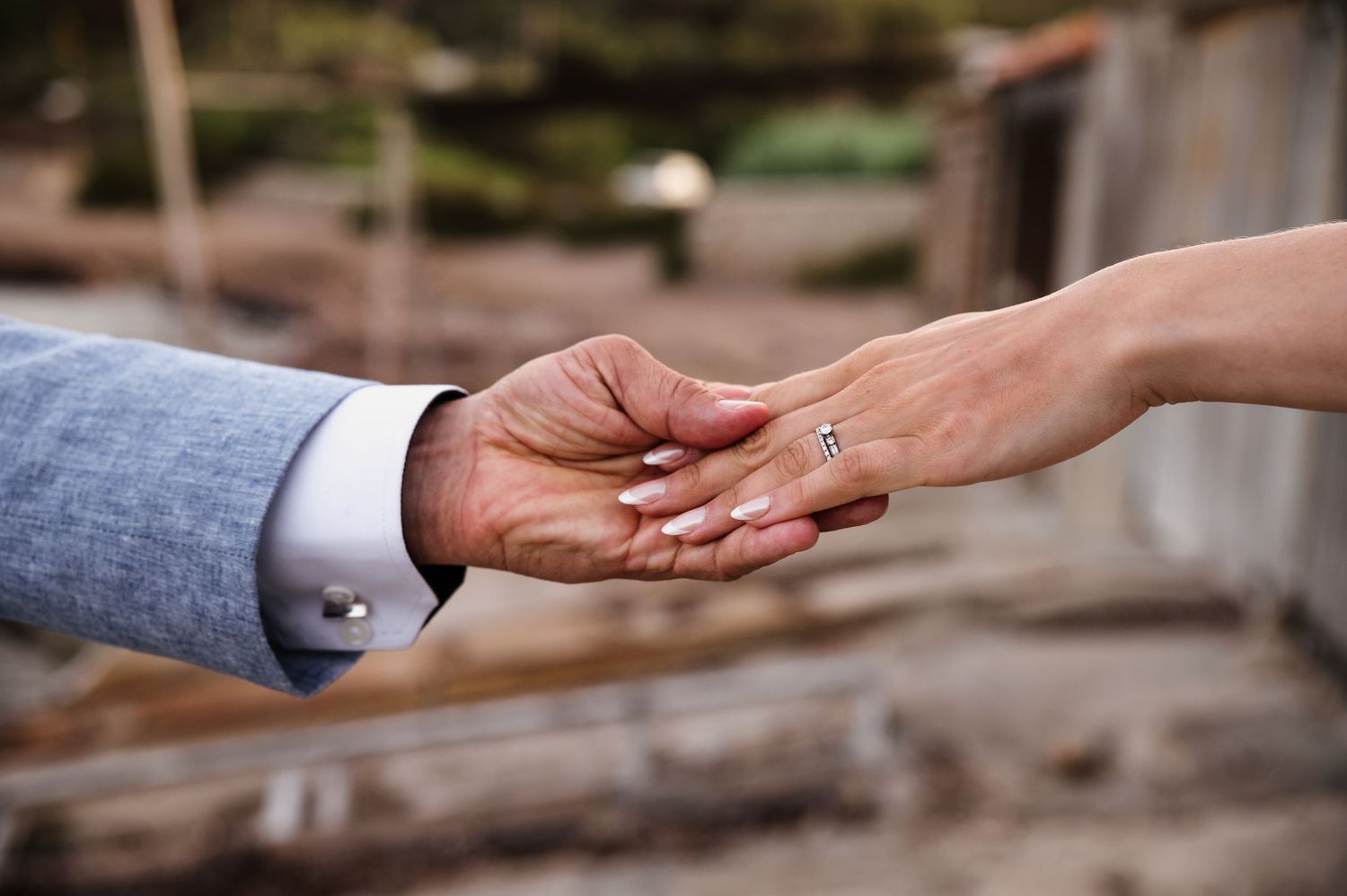 Close-up of couple holding hands, woman wearing diamond engagement ring, man in blue suit jacket.
