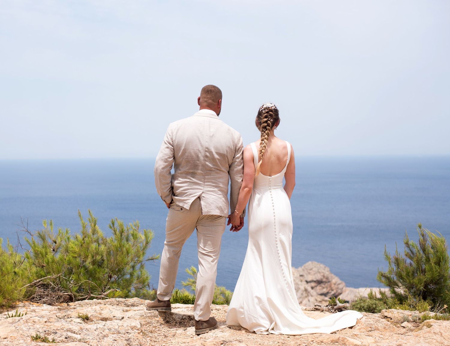 Bride and groom holding hands overlooking the ocean on a sunny day at a cliffside wedding venue.
