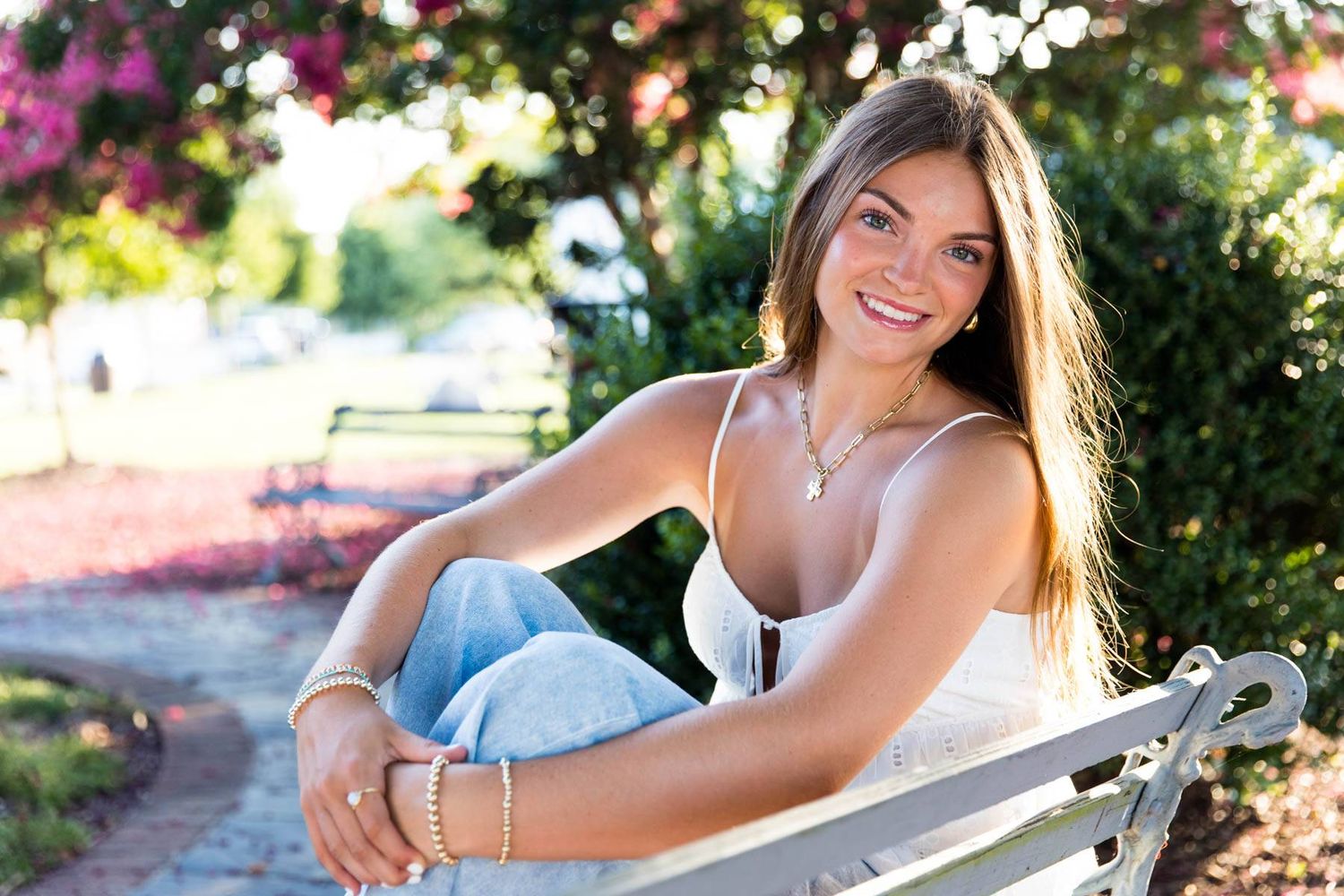 Young adult girl sitting on park bench in Ashland, Virginia. Pink flowers on tree in background. 
Senior photography RVA. Family photography