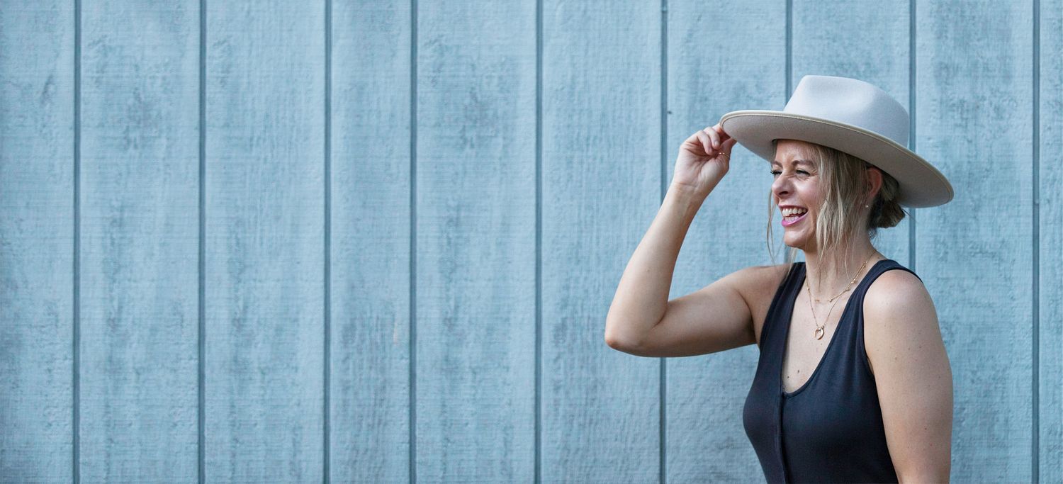 Woman in a black top and white hat against whitewashed wooden wall. Brand photography RVA, brand photography Richmond, Virginia. Headshot.