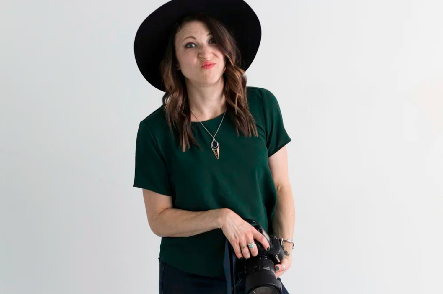Woman in a green top and black hat holding a camera. Headshot photography Richmond, VA. Headshot photography RVA. Branding photography RVA.