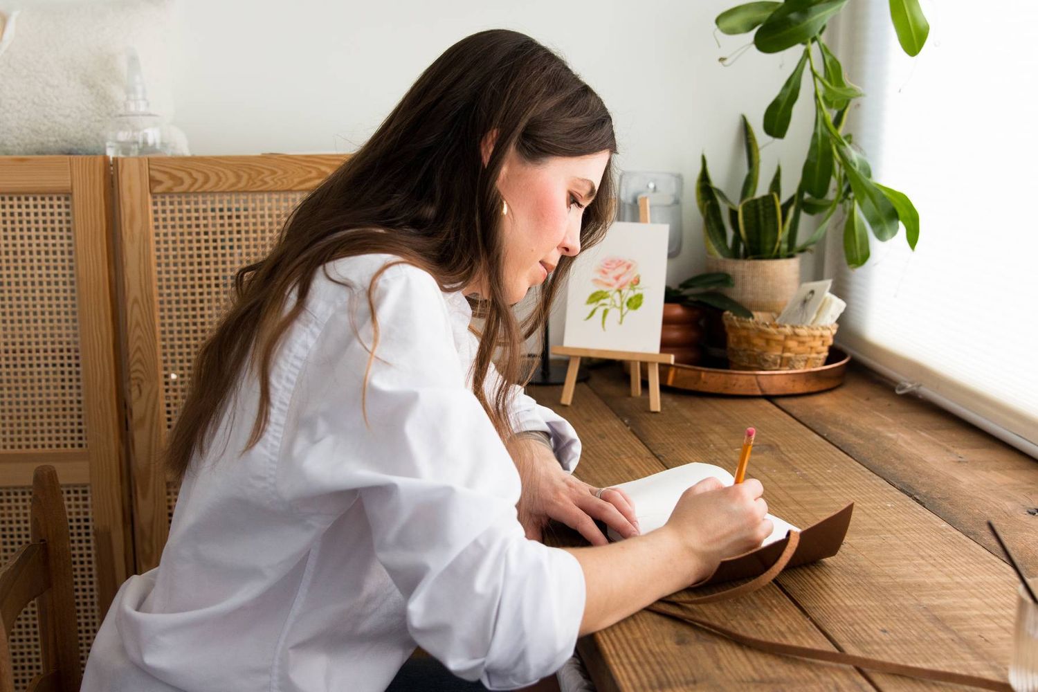 Young woman sketching in a leather sketchbook. Watercolor artist sketching designs sitting in a small studio. Brand photography RVA.