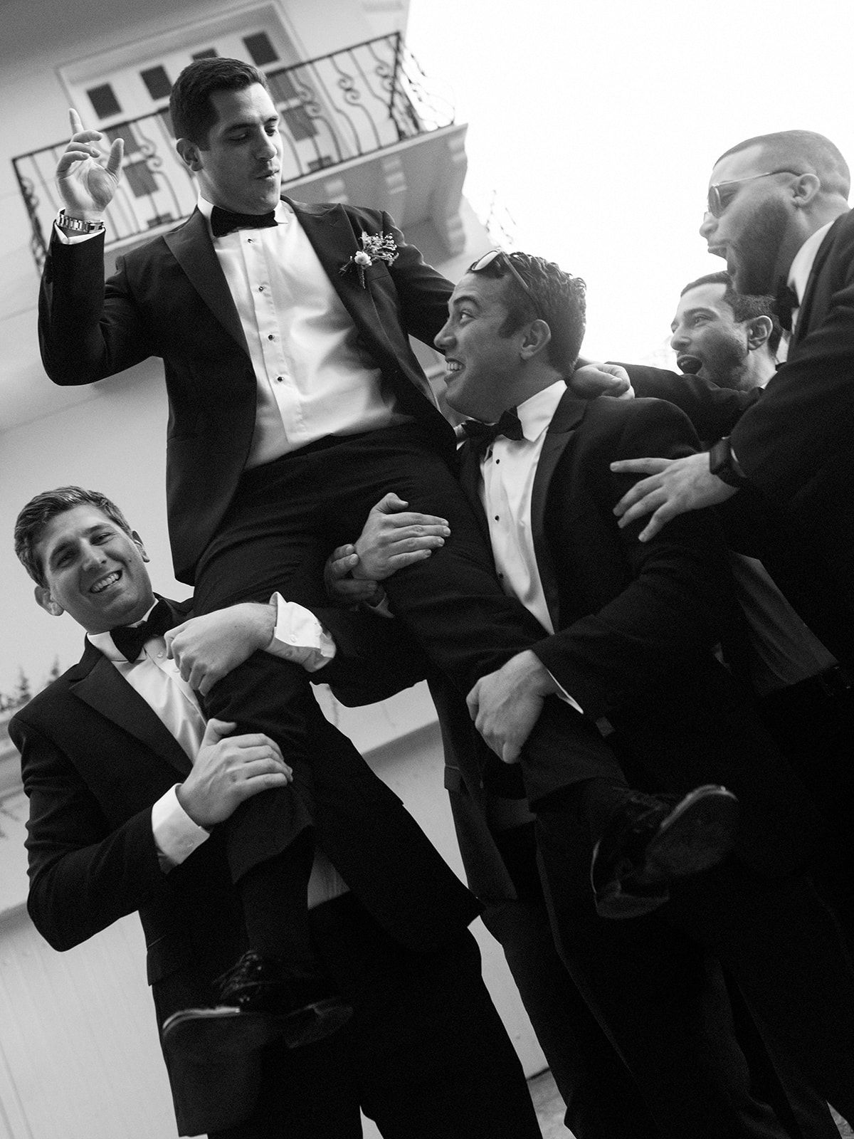 Groomsmen in tuxedos having fun and laughing during a candid black and white moment.