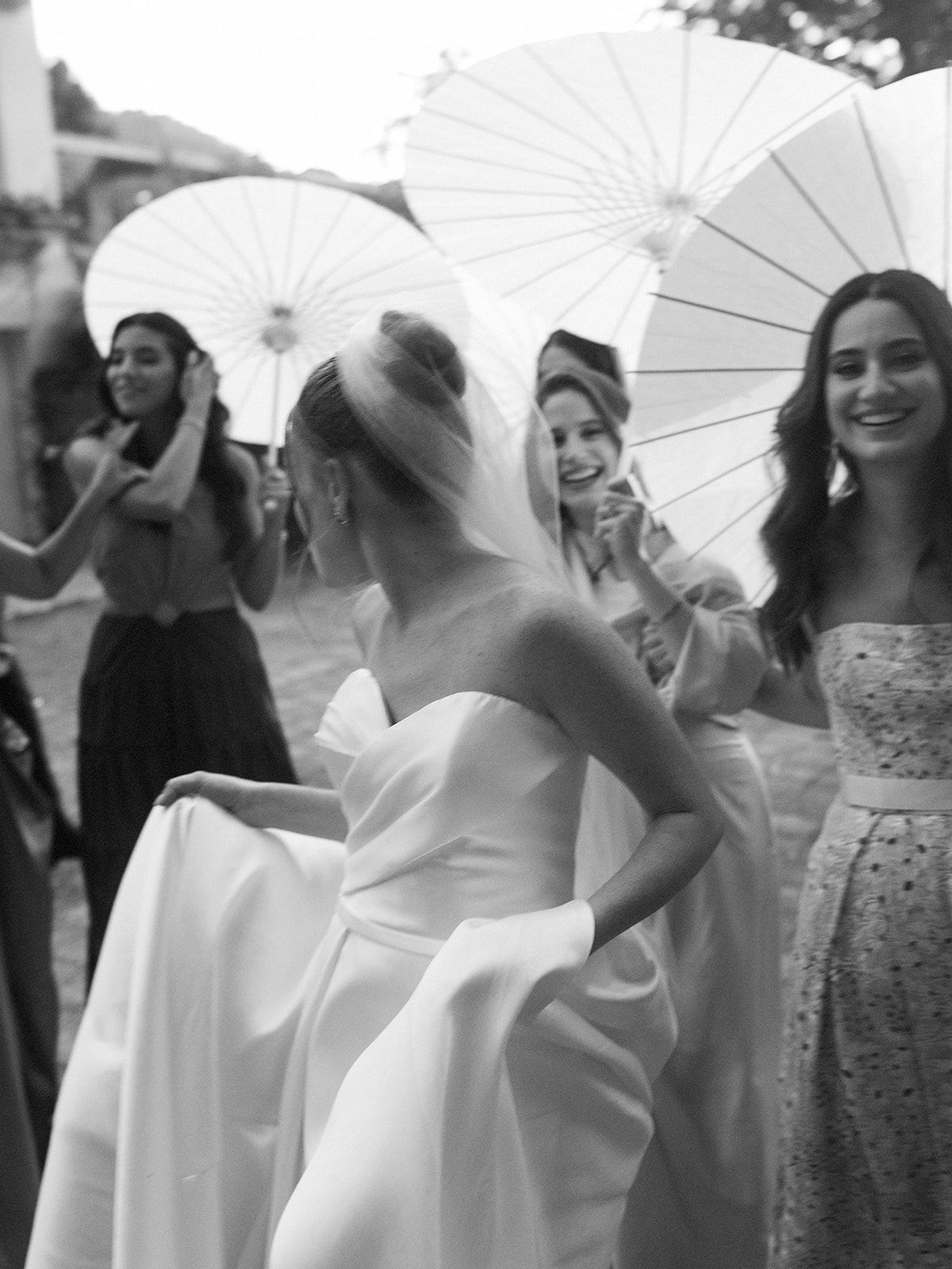 Wedding party with white parasols gathered outdoors in elegant black and white photography.
