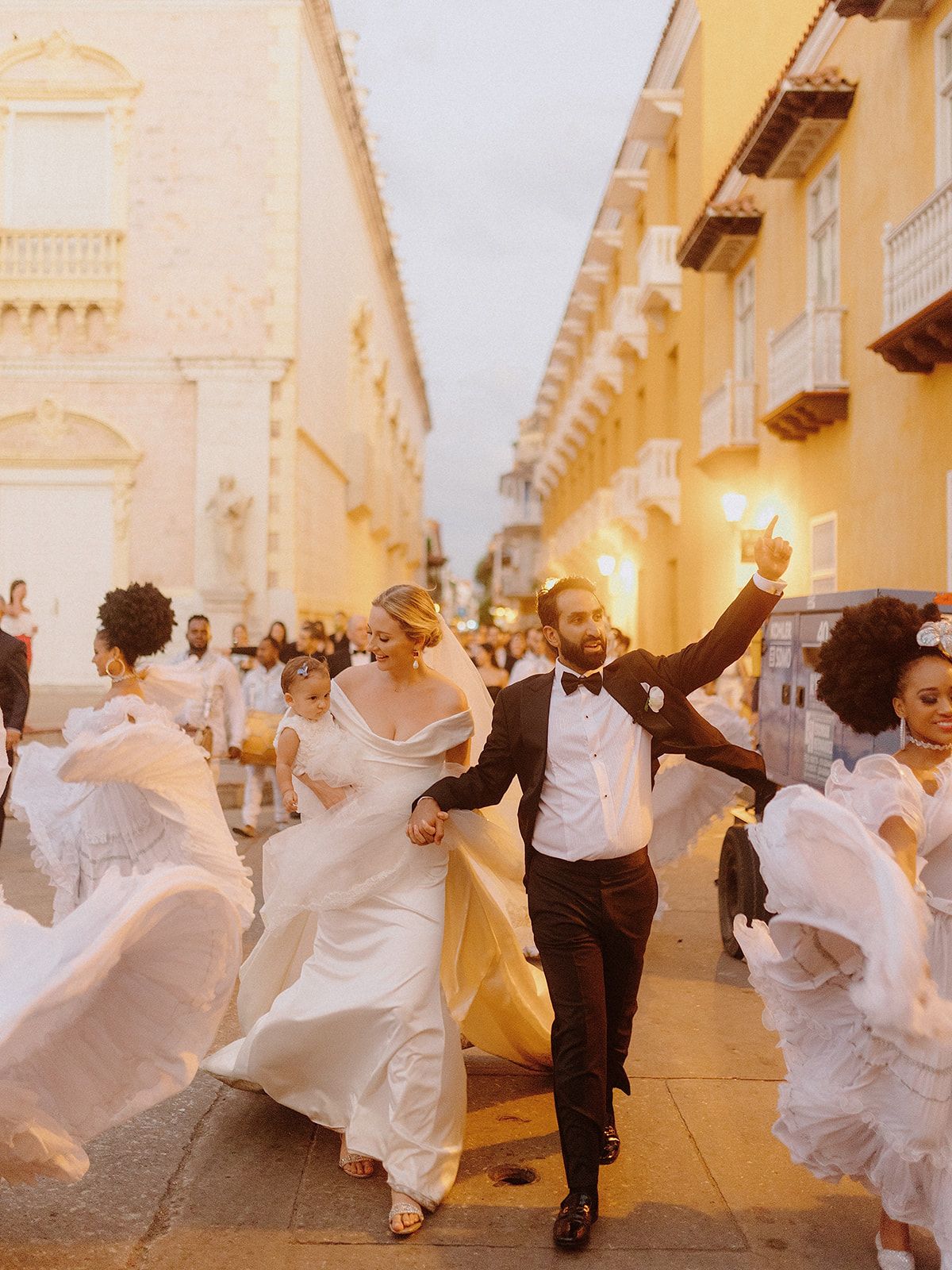 Joyful wedding party dancing and celebrating in the streets of a historic yellow-walled city.