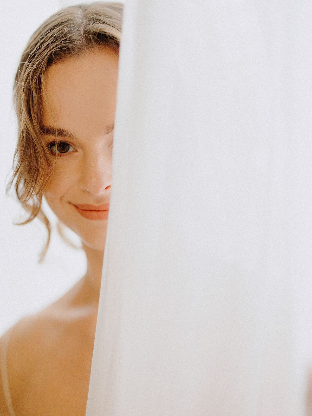 Artistic bridal portrait partially hidden behind sheer white fabric.