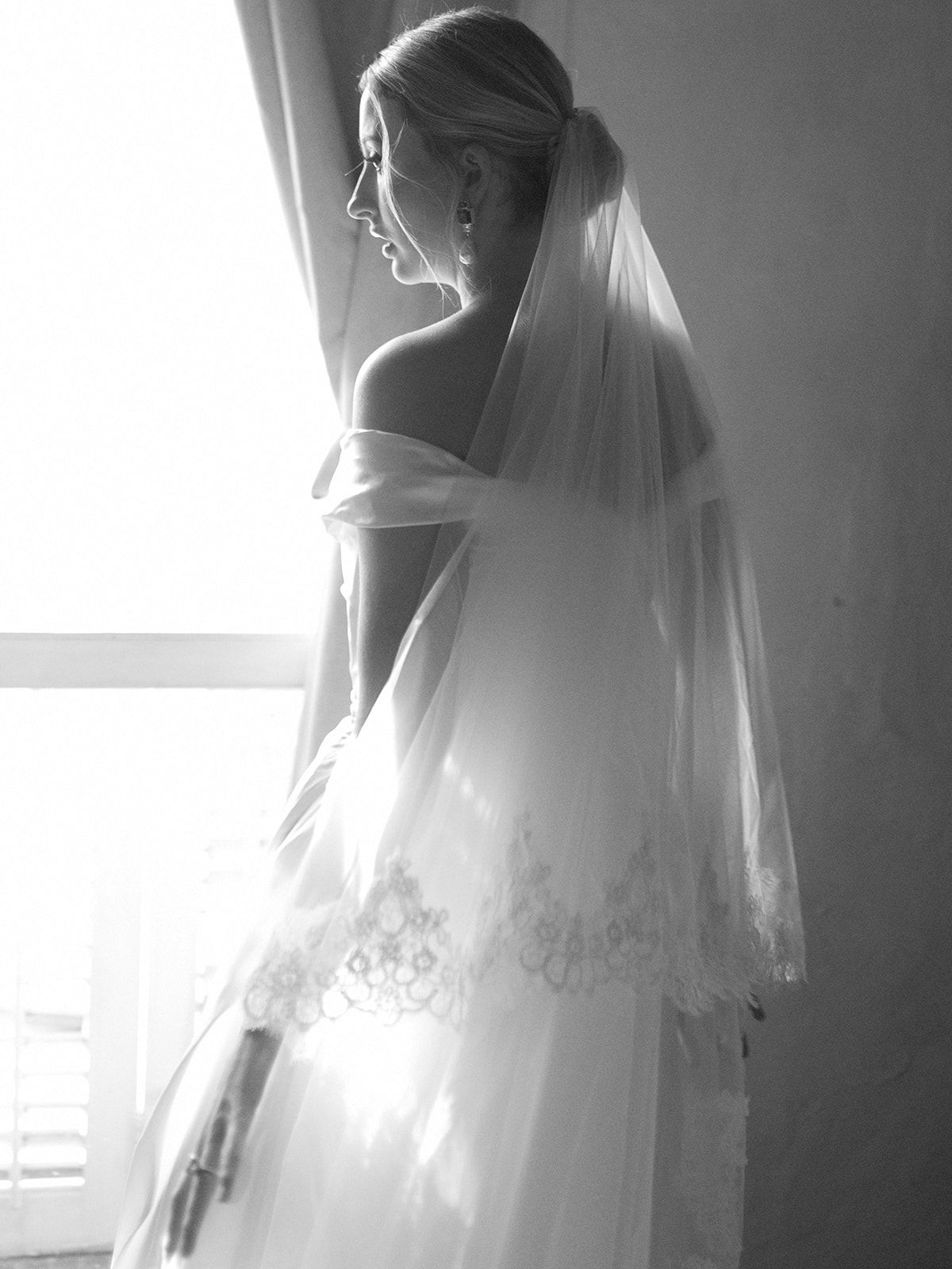 A dramatic backlit black and white portrait of a bride in her wedding gown and veil.