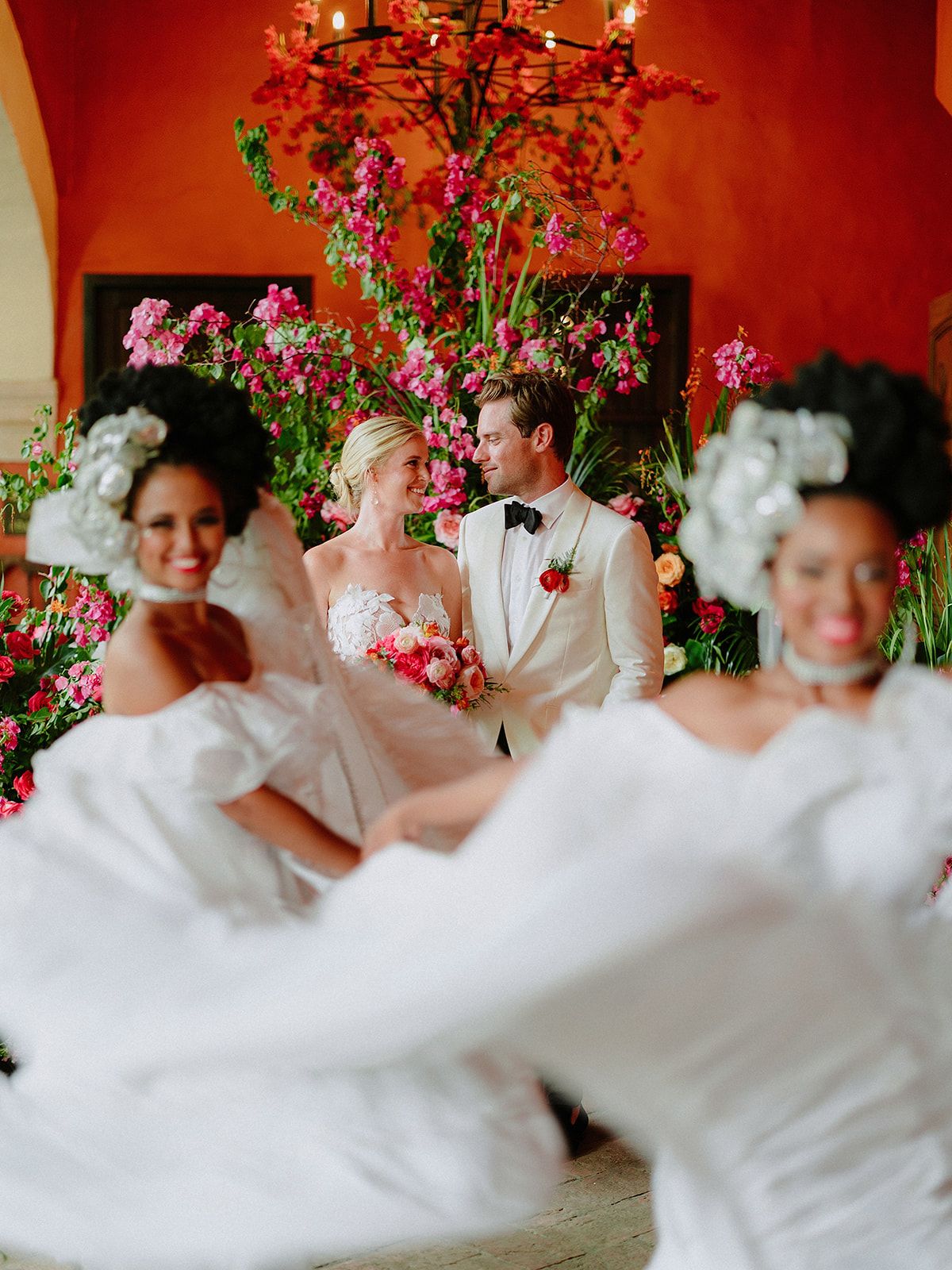 Wedding celebration with pink floral arrangements against a vibrant red wall.