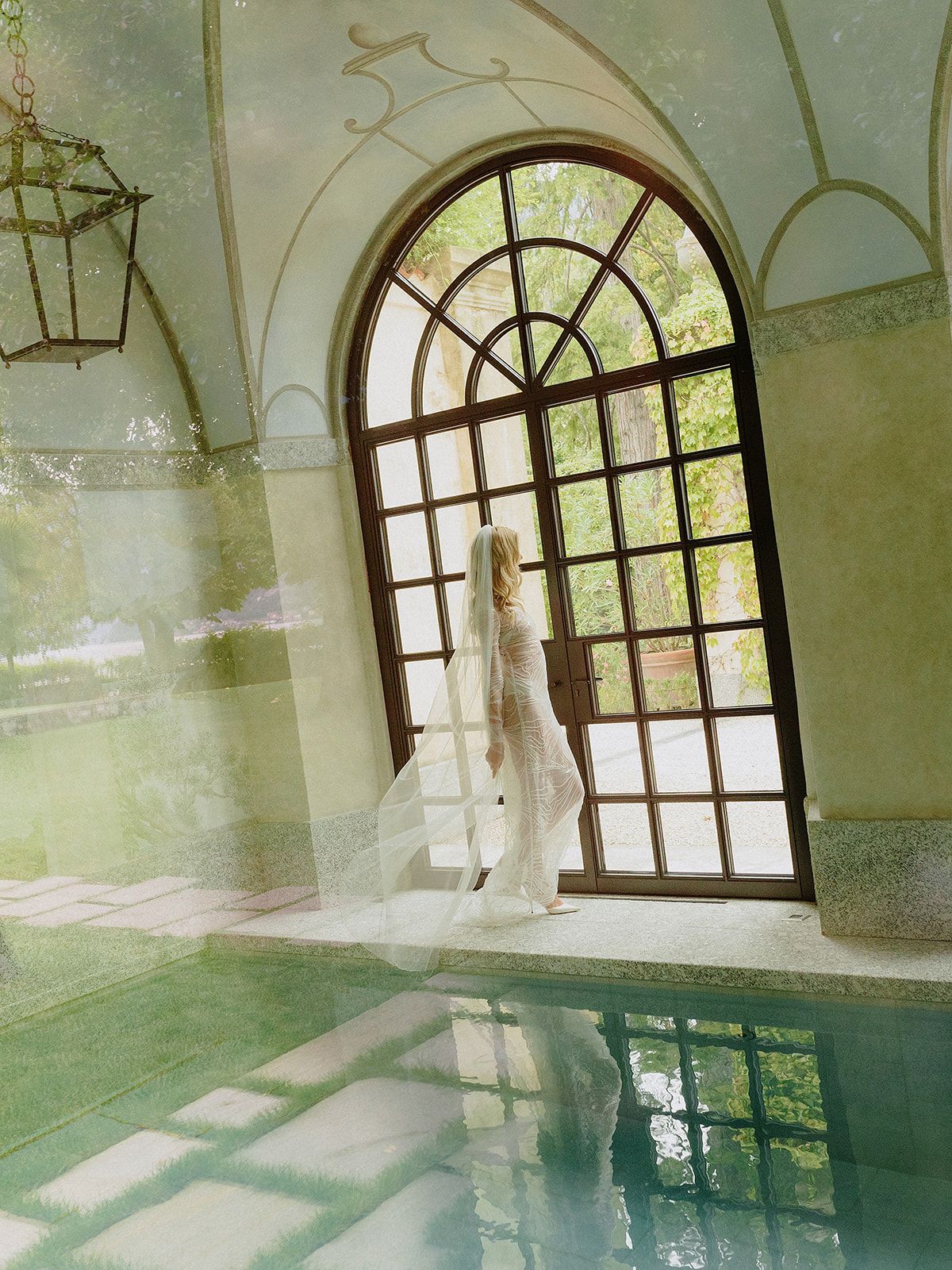 Ethereal bridal portrait by an arched window overlooking an indoor pool.