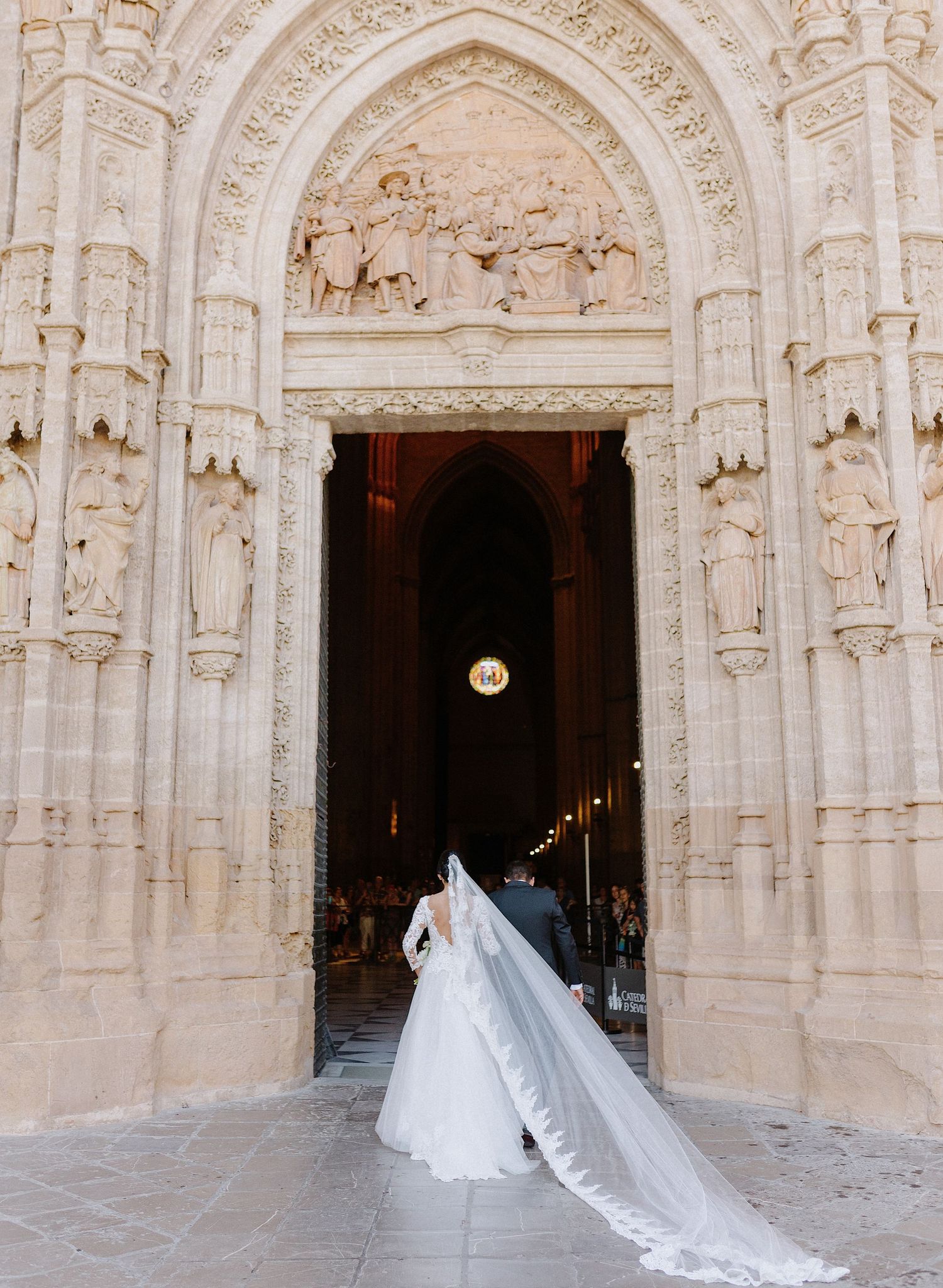 Cathedral entrance with ornate stone archway and flowing white wedding veil.
