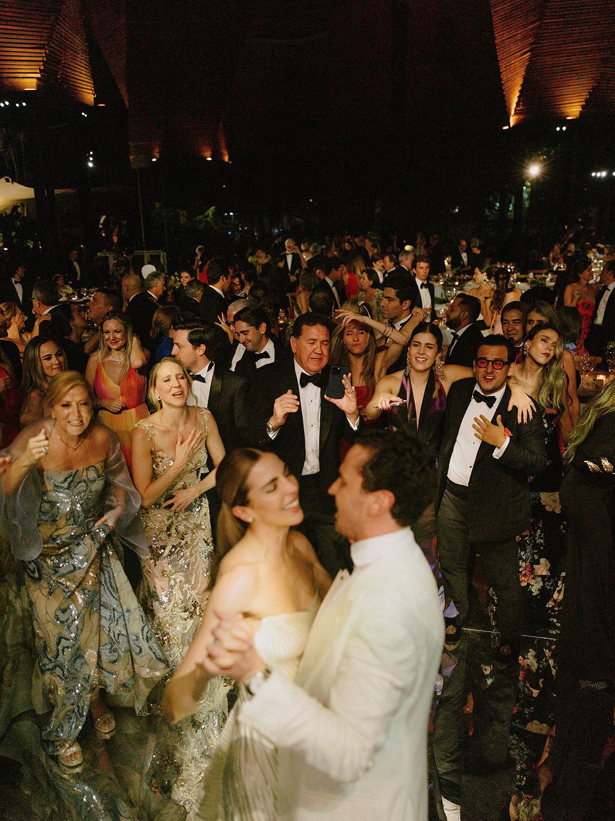 Crowded wedding dance floor with guests celebrating under warm lighting.