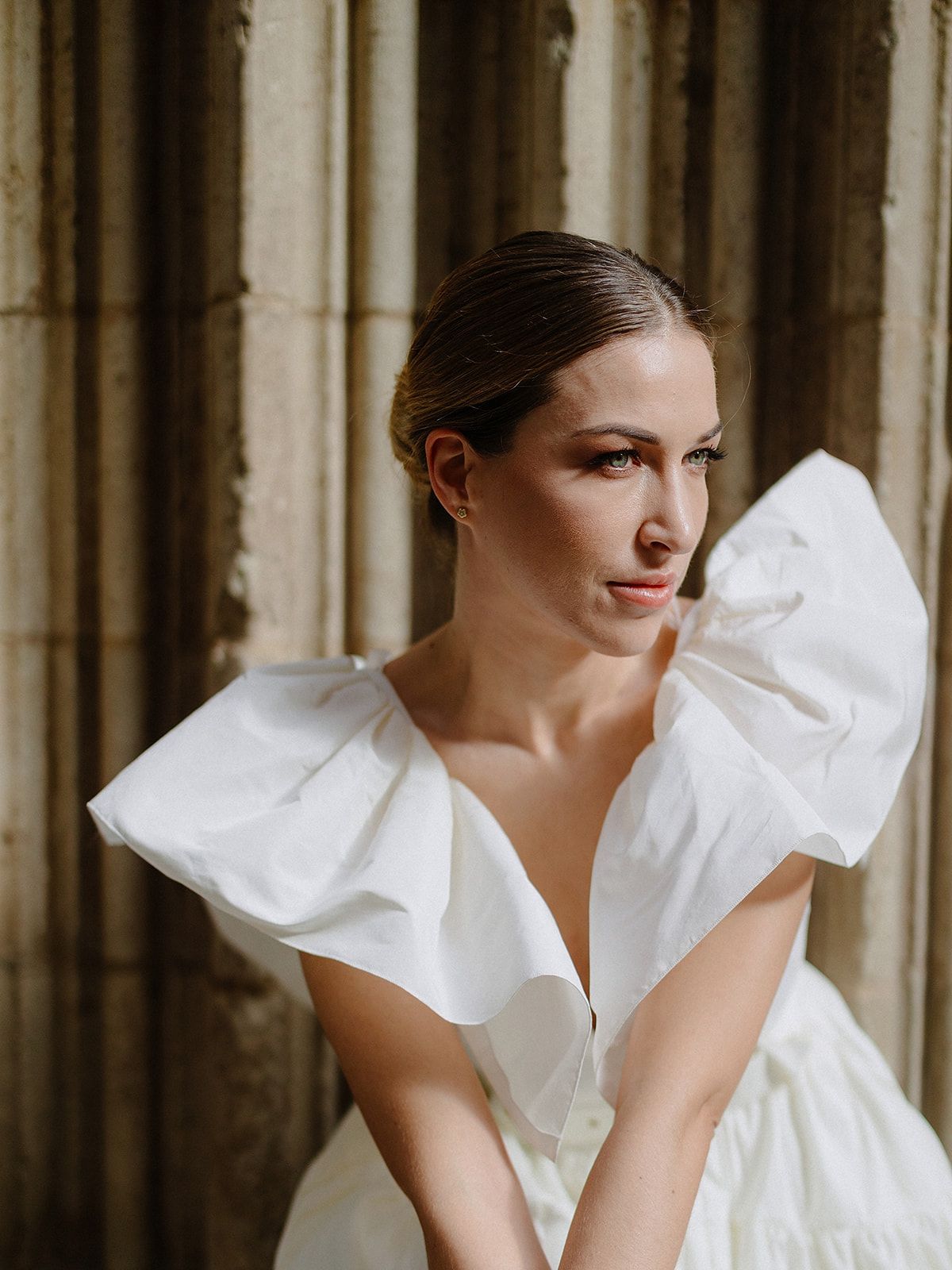 A white bridal gown with dramatic ruffled sleeves photographed against stone columns.