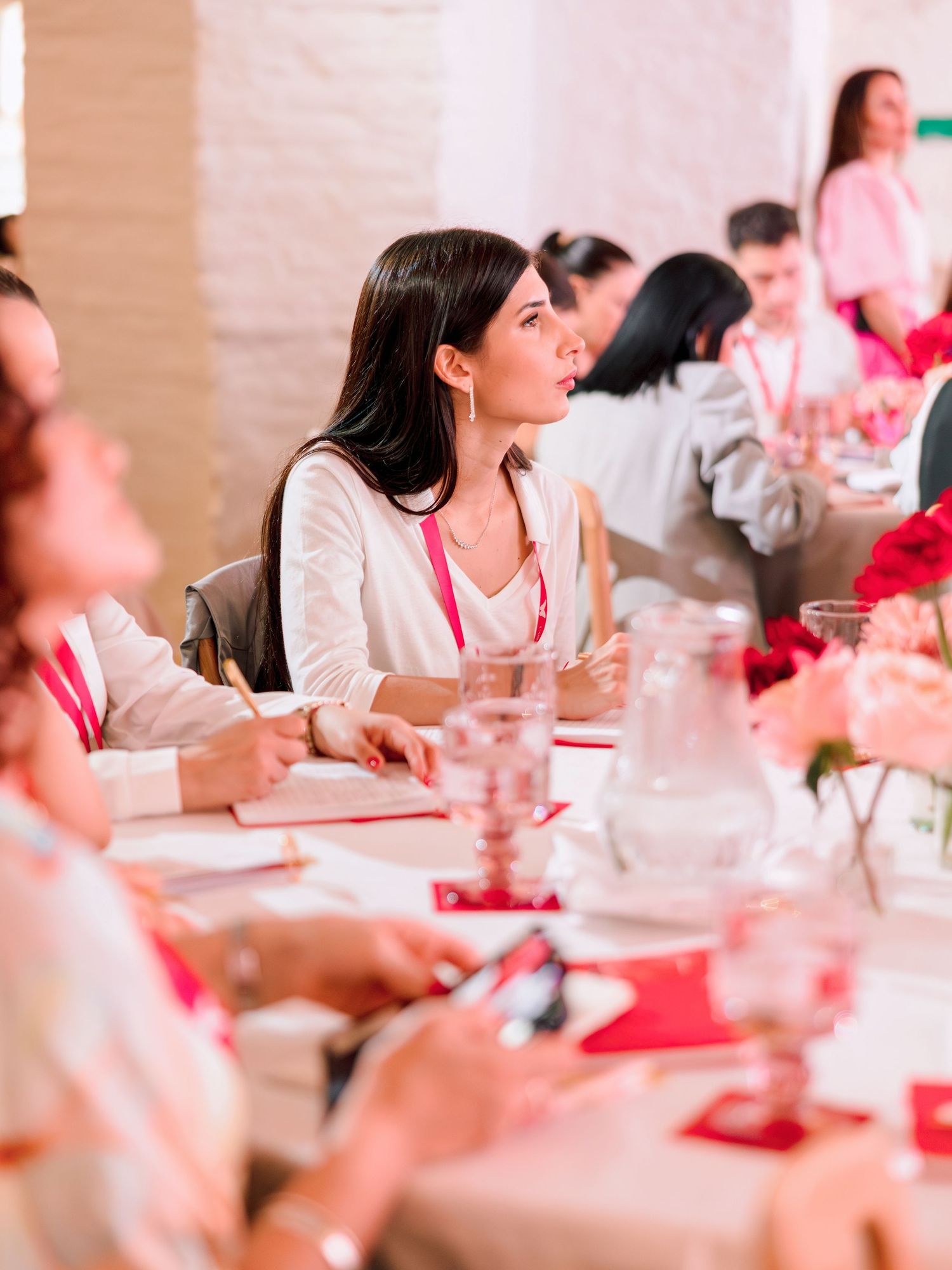 People seated at a dining table during a social gathering with pink and white decor elements in view.