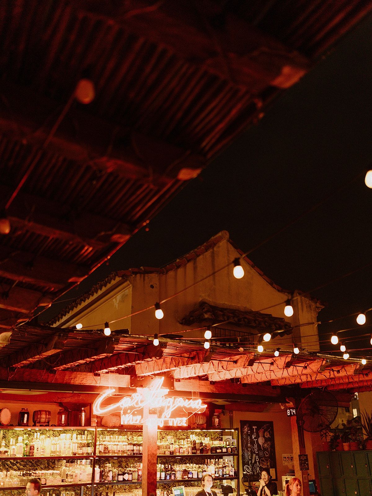 Warm-lit bar interior with hanging string lights and exposed ceiling beams creating a cozy atmosphere.