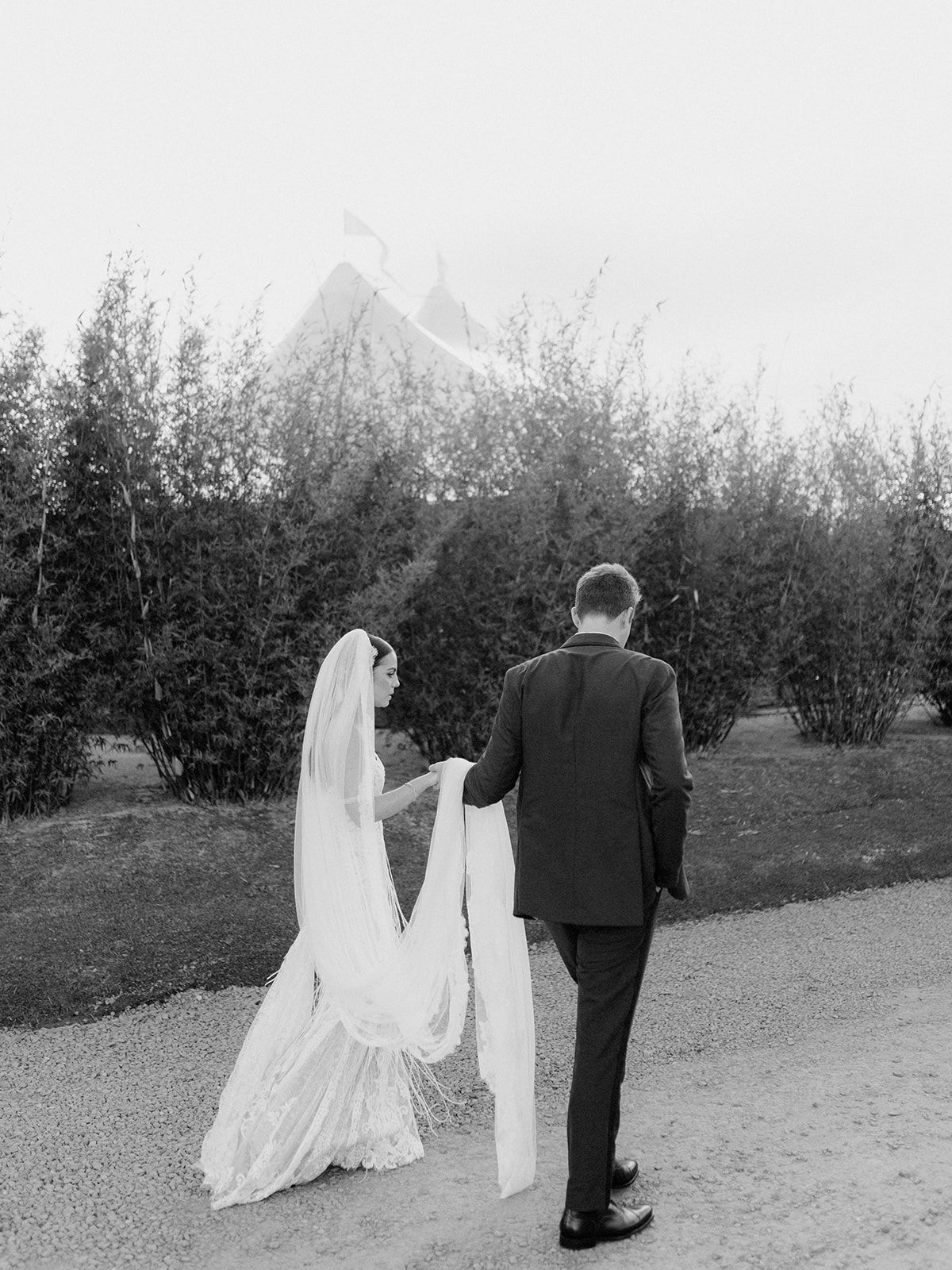 A black and white wedding photo of a couple walking down a garden path.