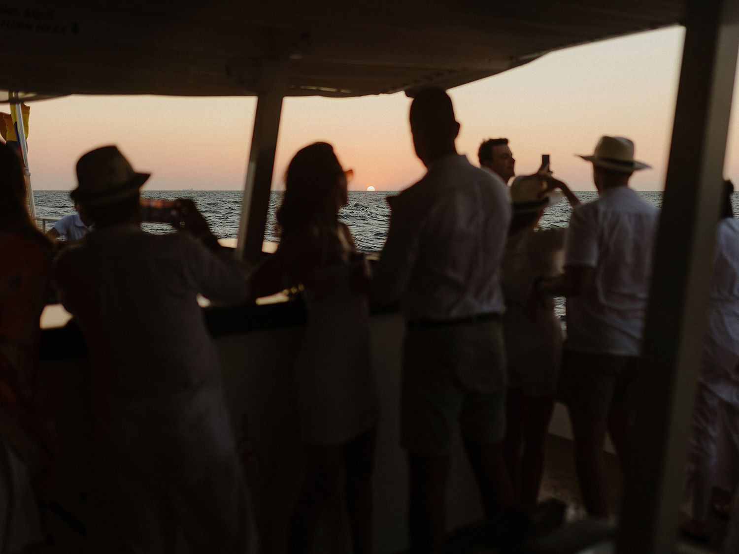 Silhouettes of people enjoying a sunset boat ride on the ocean.