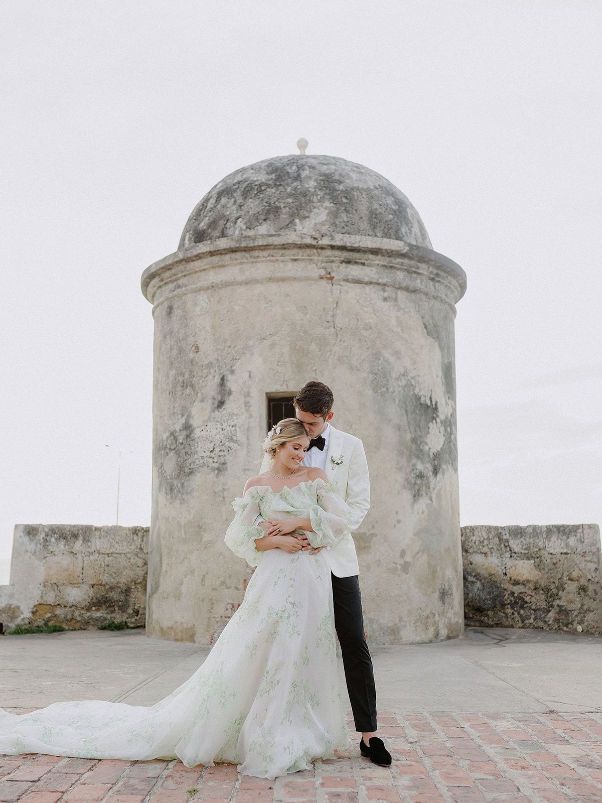 A romantic wedding portrait in front of a weathered stone watchtower with domed architecture.