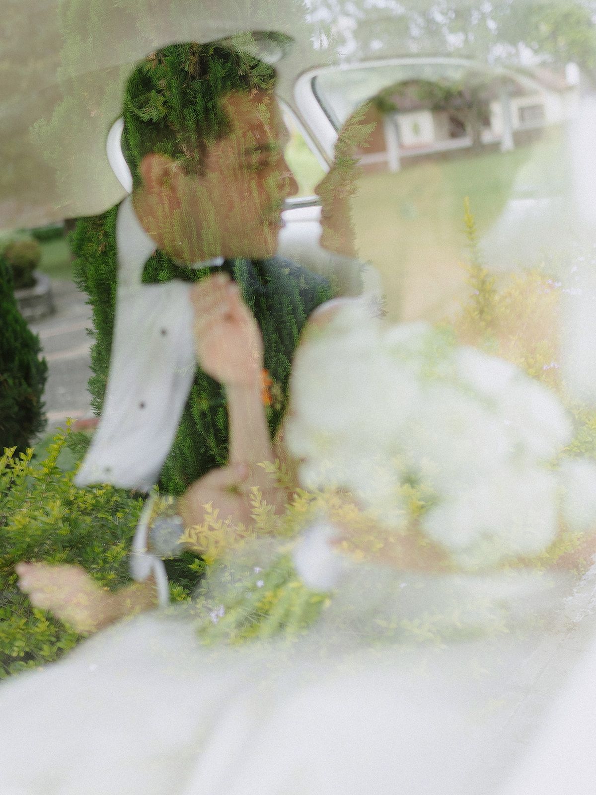 Romantic wedding couple sitting in a car with dreamy double exposure through window and greenery.
