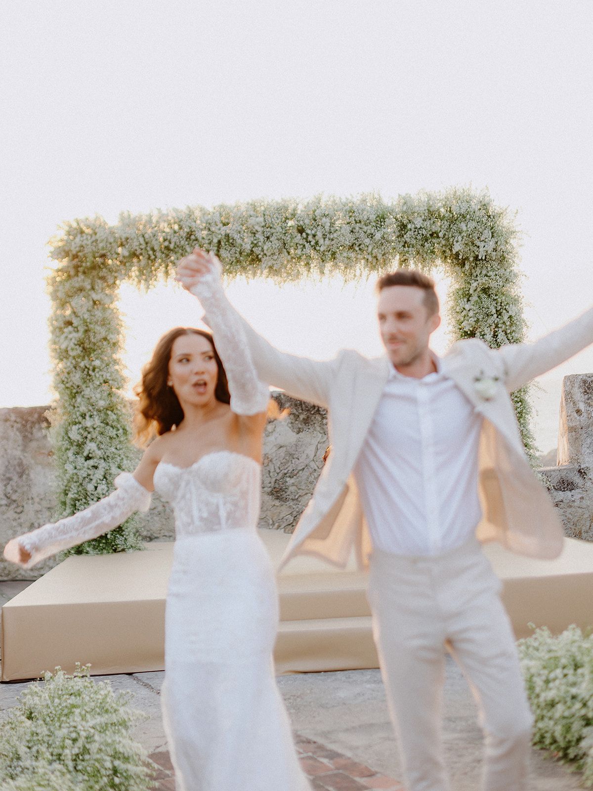 Joyful celebration under a floral arch during an outdoor wedding ceremony.