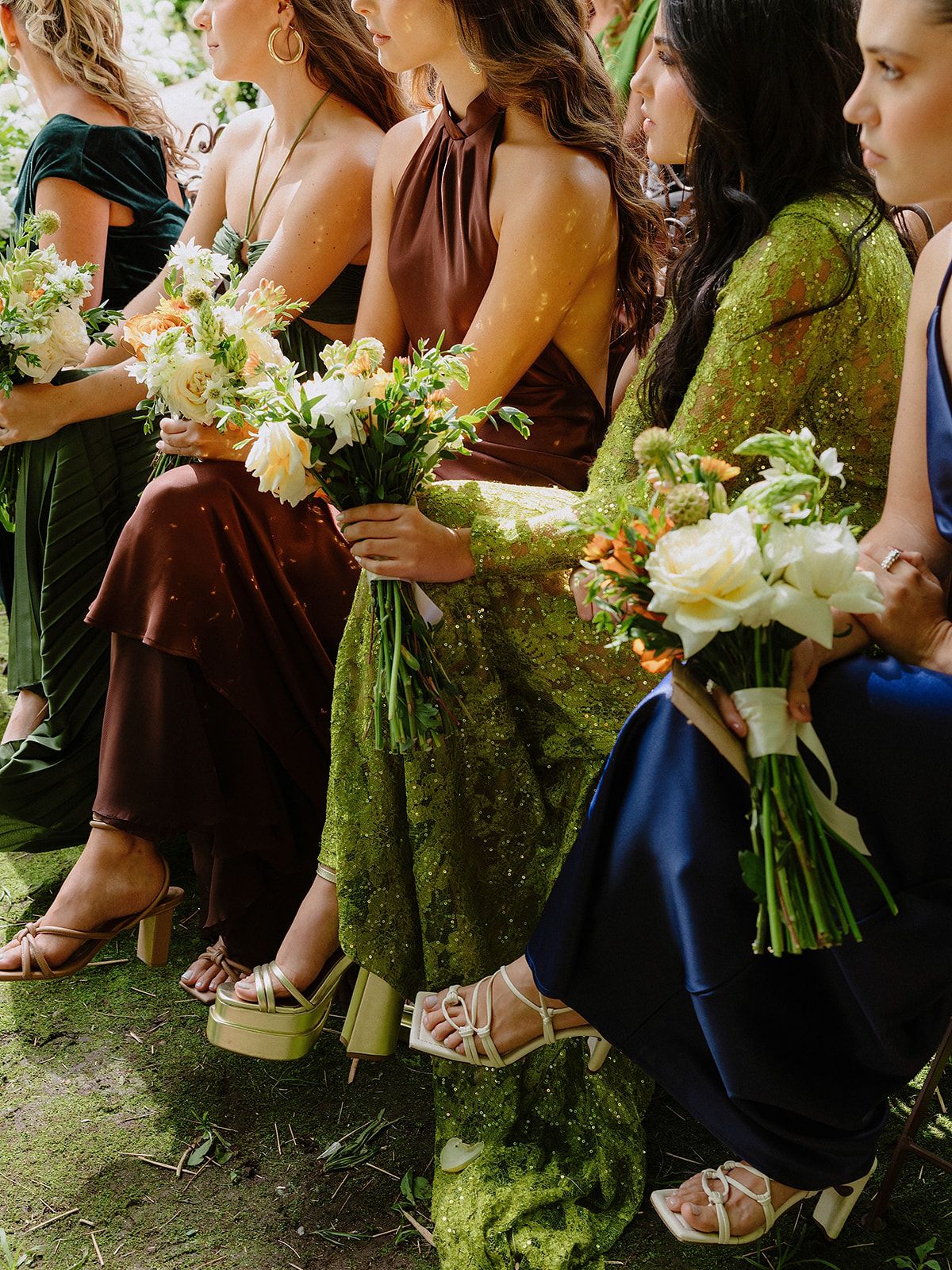 Bridesmaids in colorful dresses holding white floral bouquets during an outdoor wedding celebration.