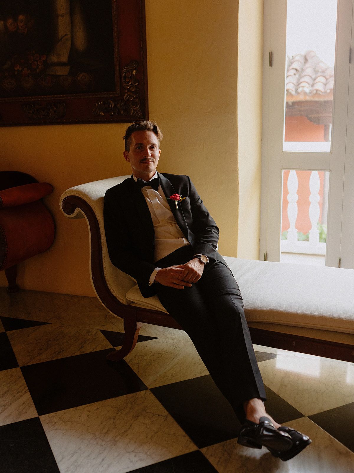 Formal portrait of a person in classic black tuxedo seated on an elegant chair.