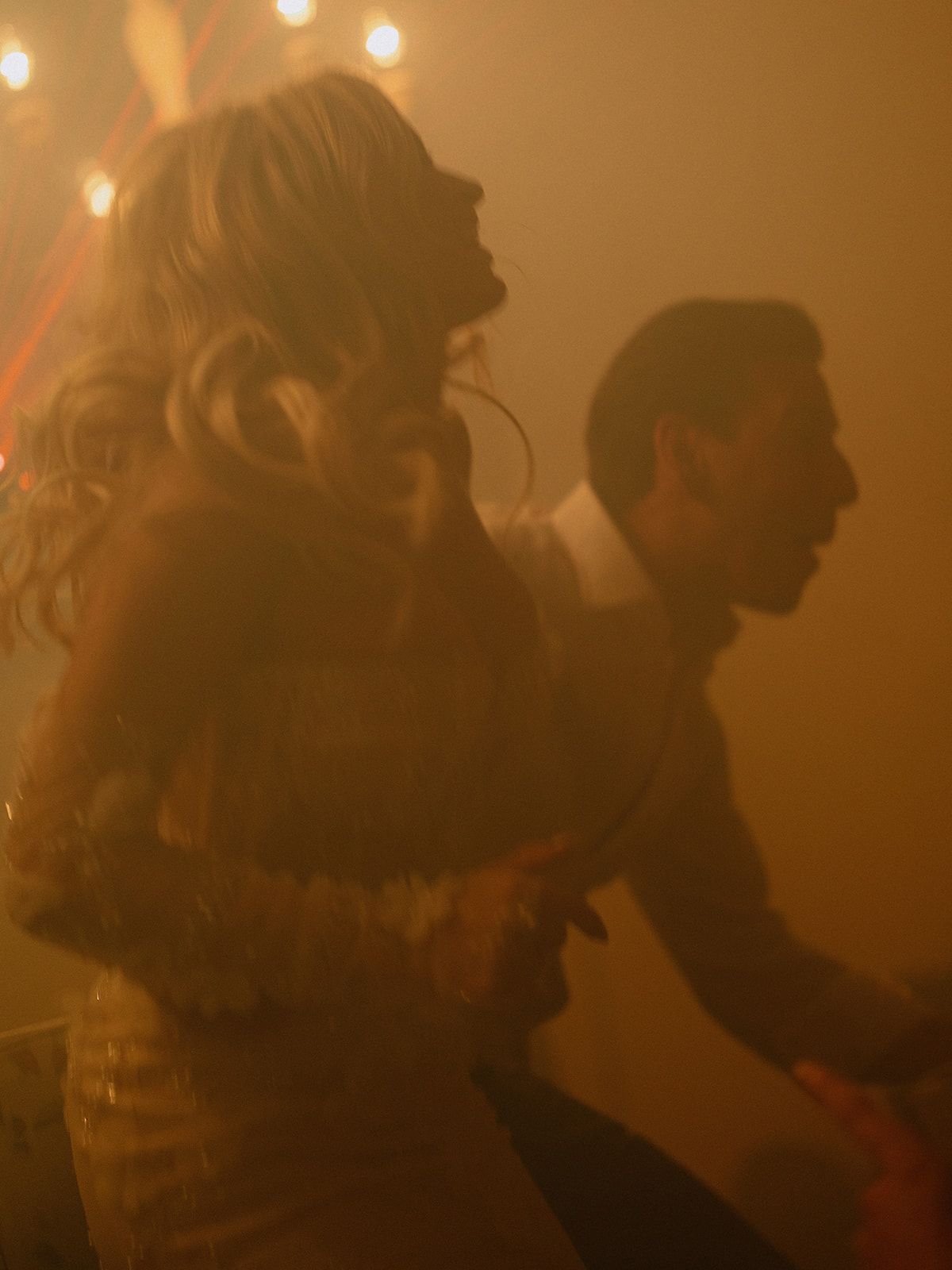 Silhouetted couple dancing in warm atmospheric lighting at wedding reception.