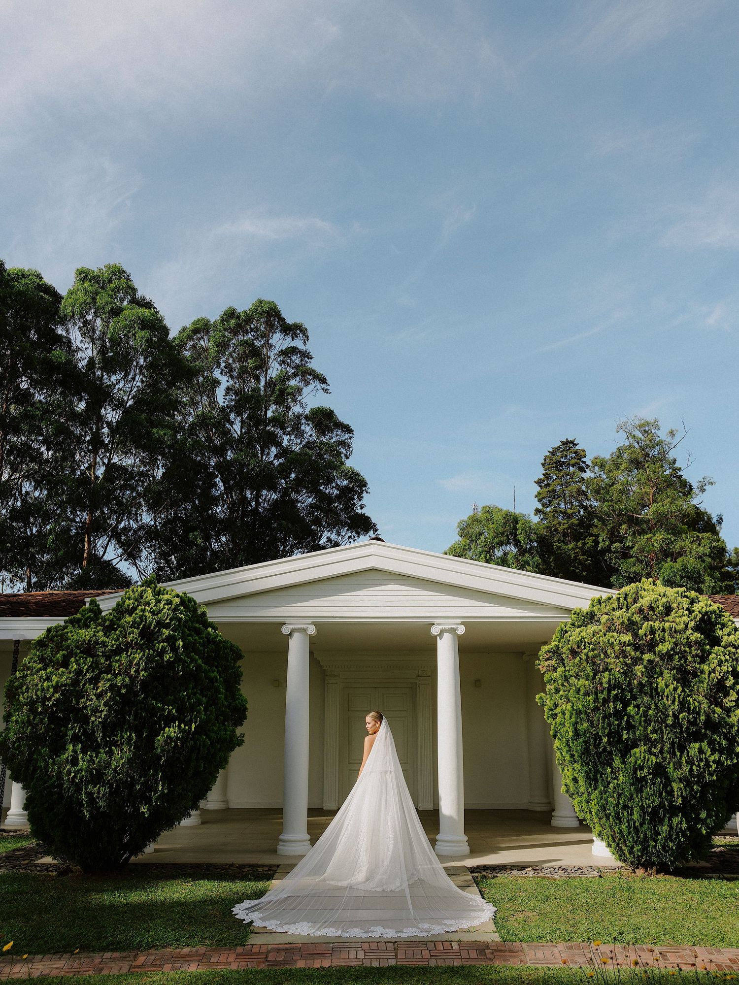 Wedding dress displayed against a classic white columned building surrounded by lush gardens.