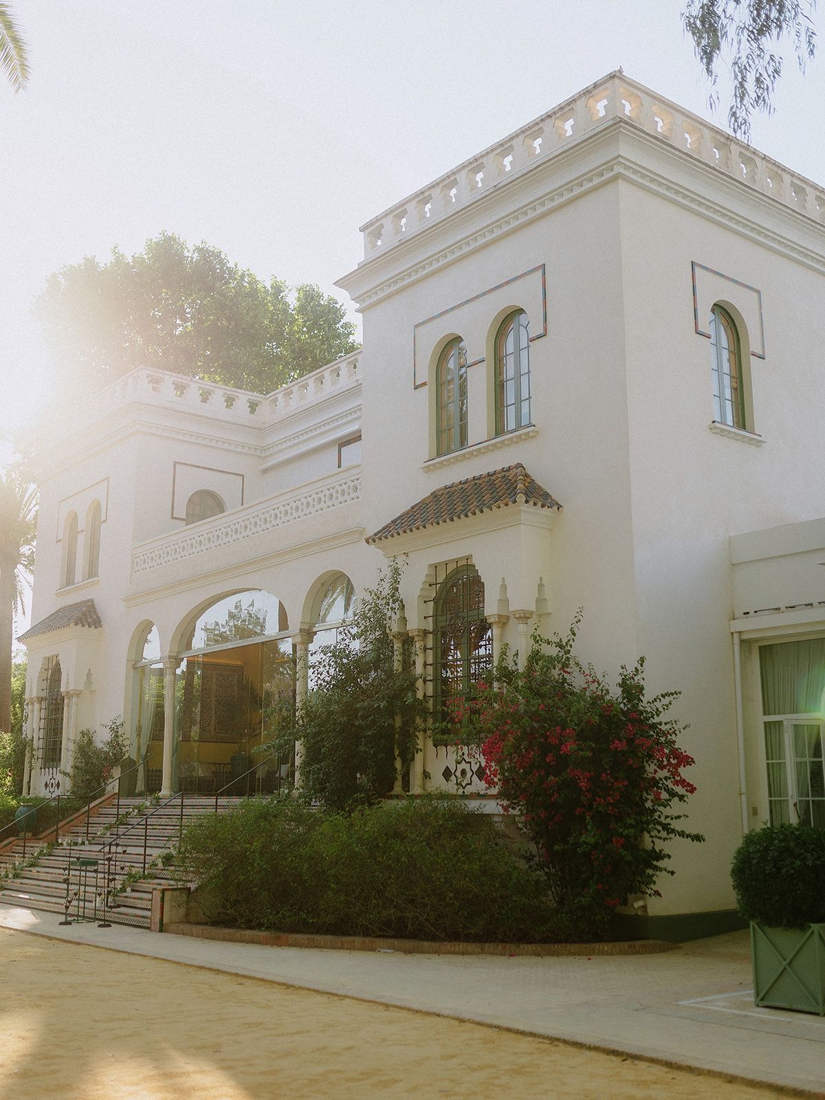 A white Spanish colonial style mansion with arched windows and red flowers in the garden.
