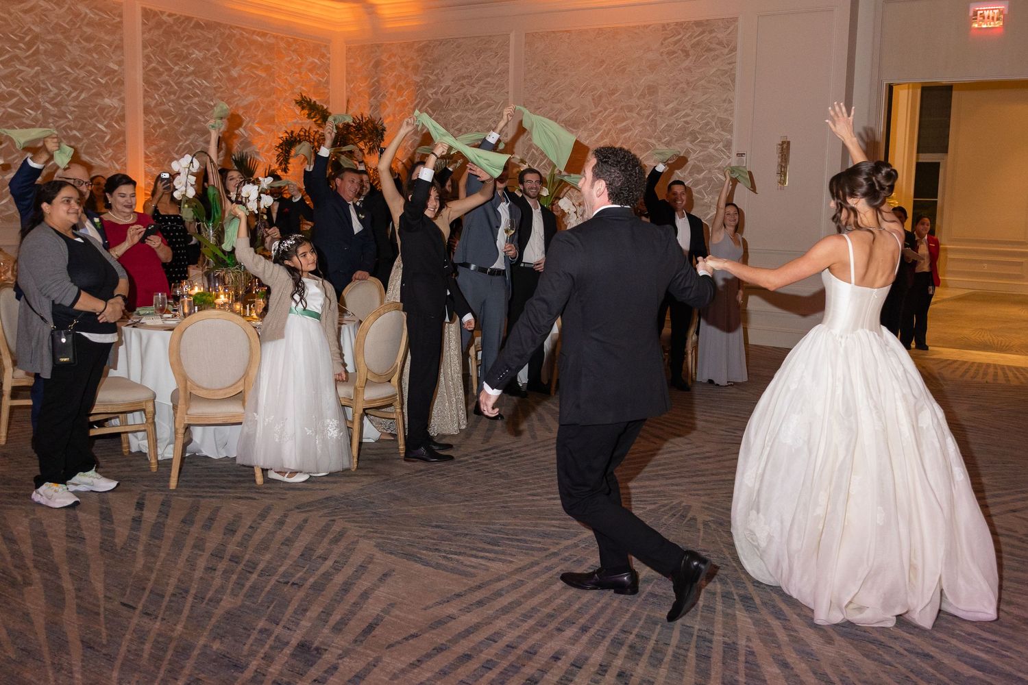 Bride and groom make grand entrance at elegant wedding reception as guests cheer and wave green fans.