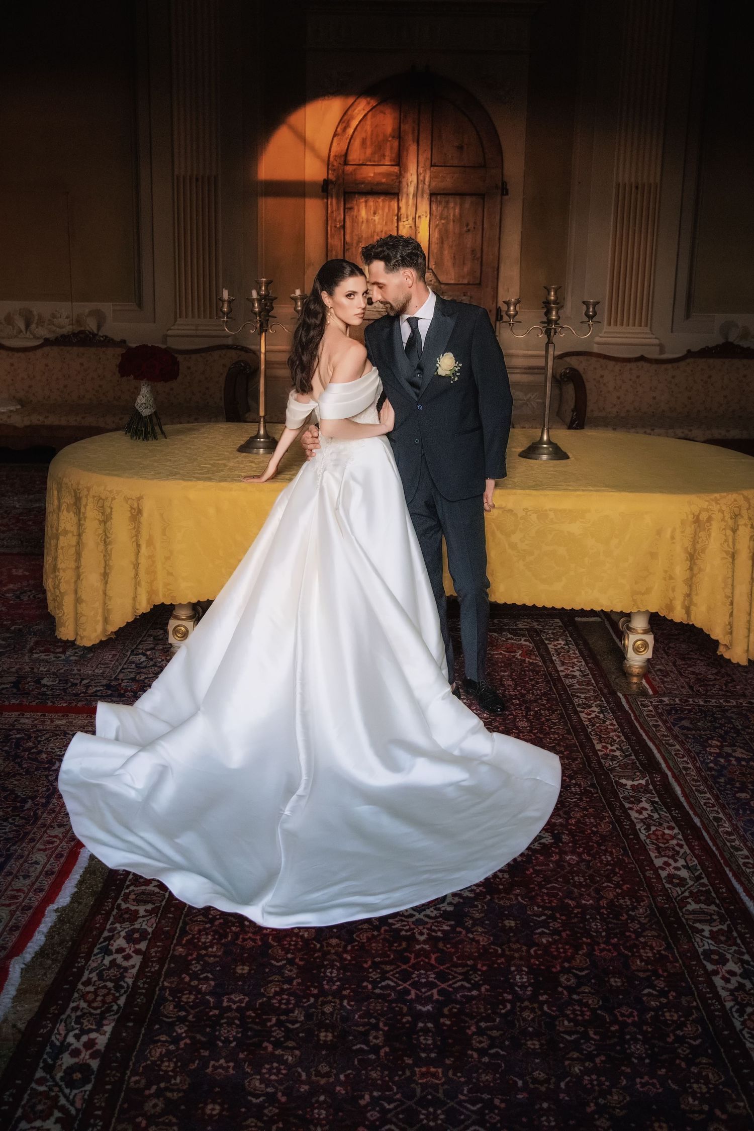 Bride and groom share an intimate dance moment on an ornate carpet in a dimly lit ballroom.