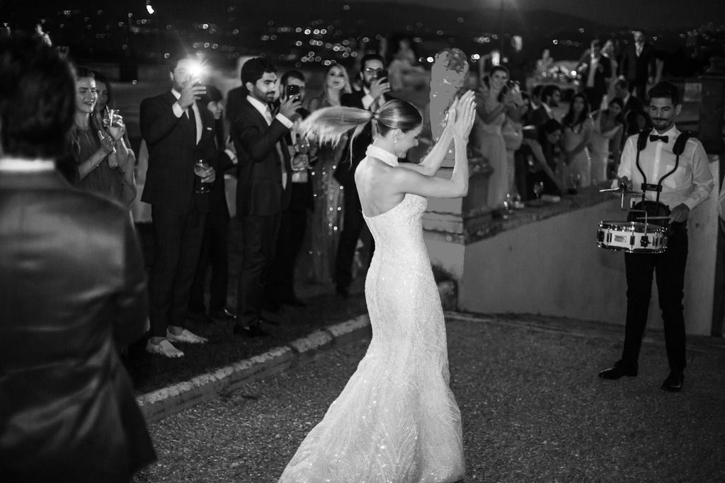 A couple shares their first dance at an outdoor evening wedding reception while guests watch and take photos.
