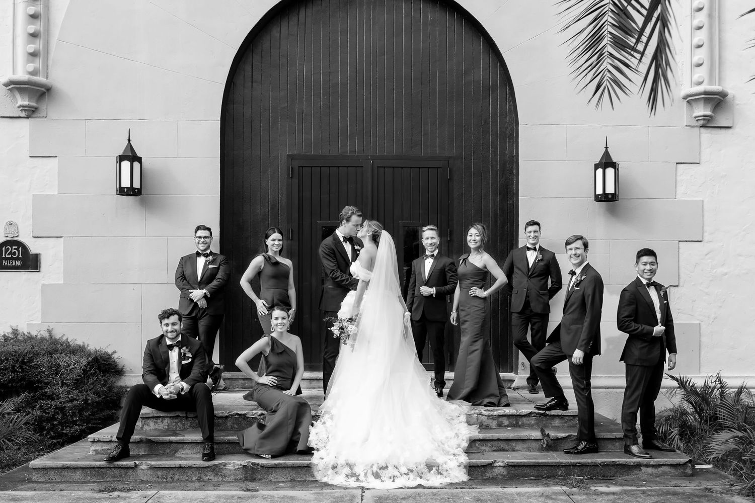 Wedding party poses dramatically in black and white under arched doorway with lanterns.