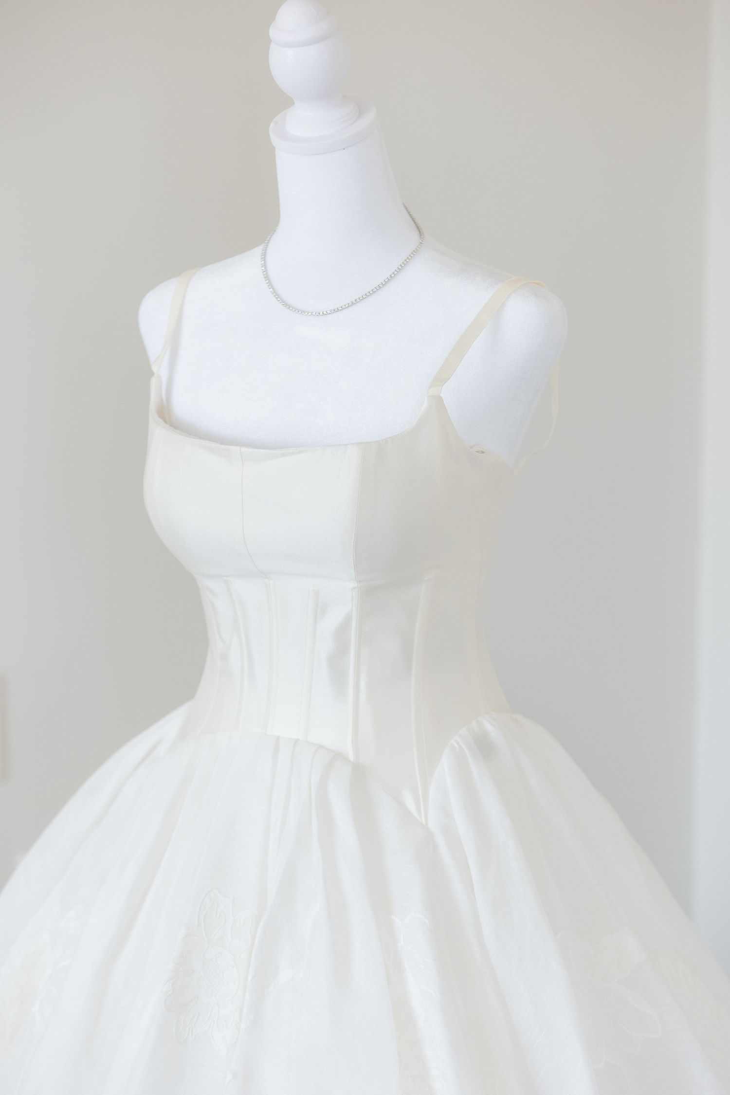 Elegant white bridal ball gown with corset bodice and spaghetti straps displayed on a mannequin.