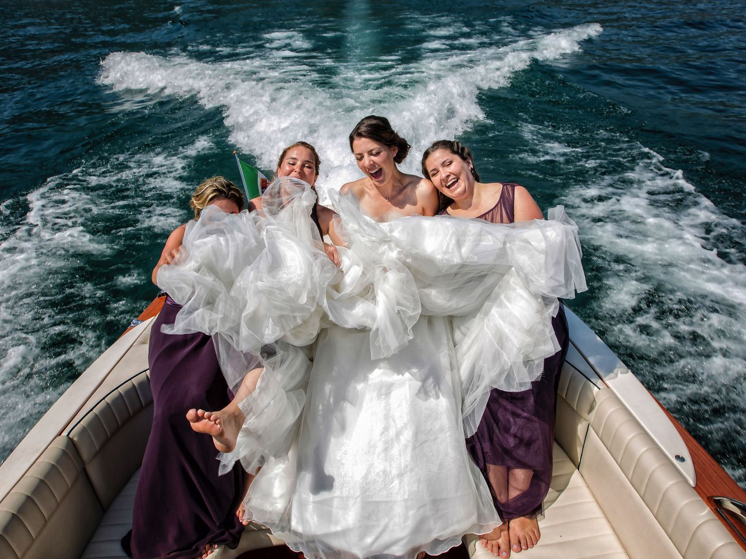 Wedding party enjoying a boat ride with white dress billowing in the ocean breeze.