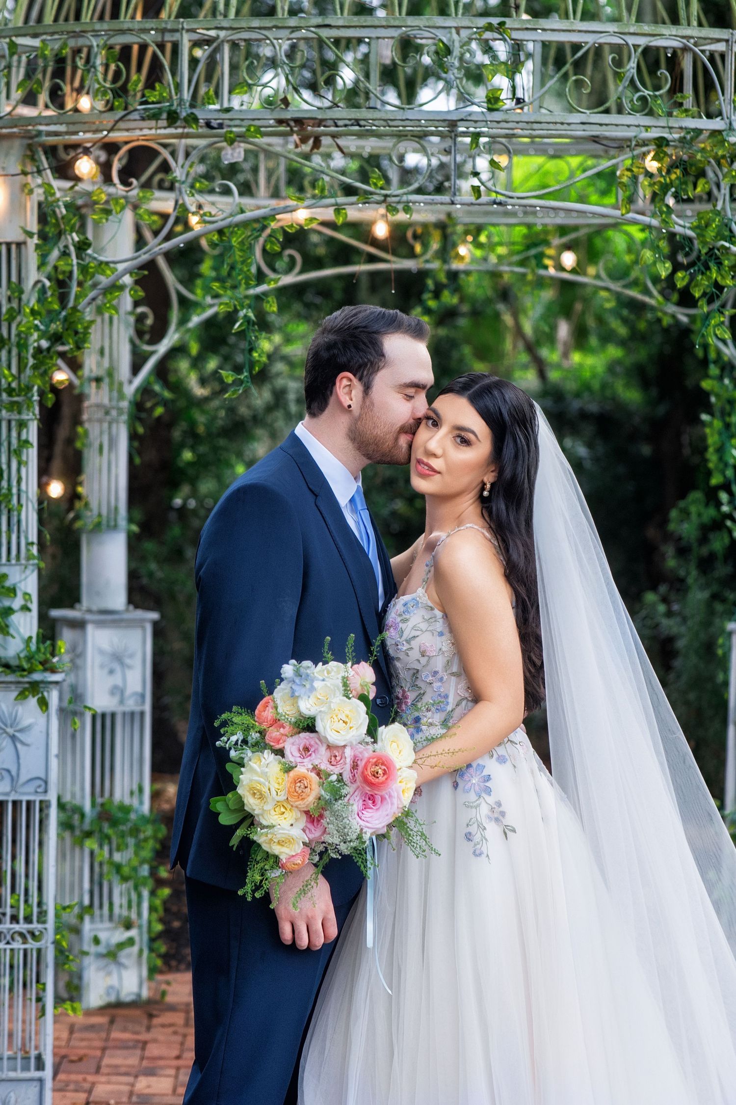 Romantic wedding portraits captured under an elegant garden arbor with flowing veil and colorful bouquet.