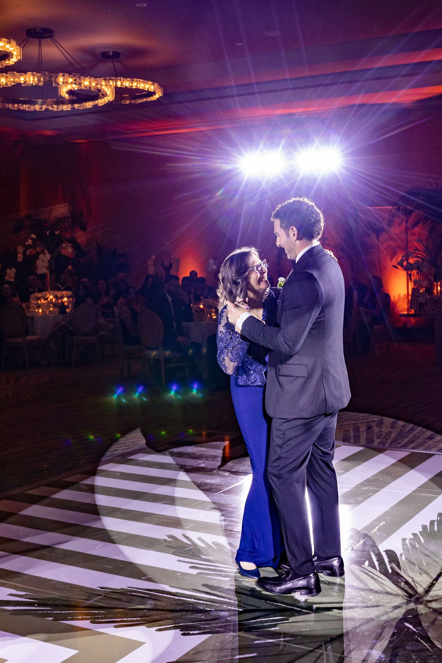 Couple sharing first dance on black and white dance floor at elegant wedding reception with dramatic stage lighting.