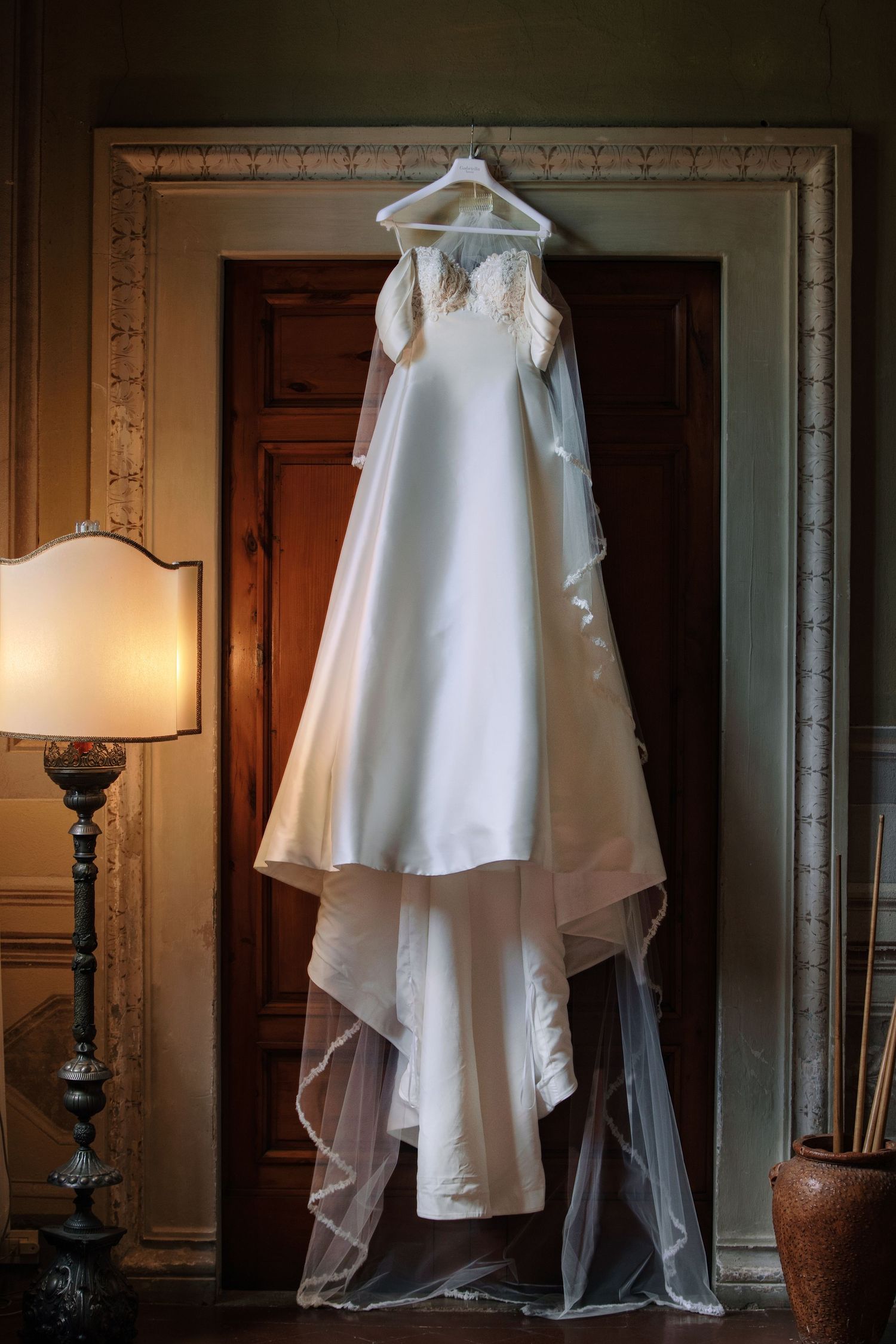 Classic white wedding dress with lace details hanging in elegant room with vintage decor.