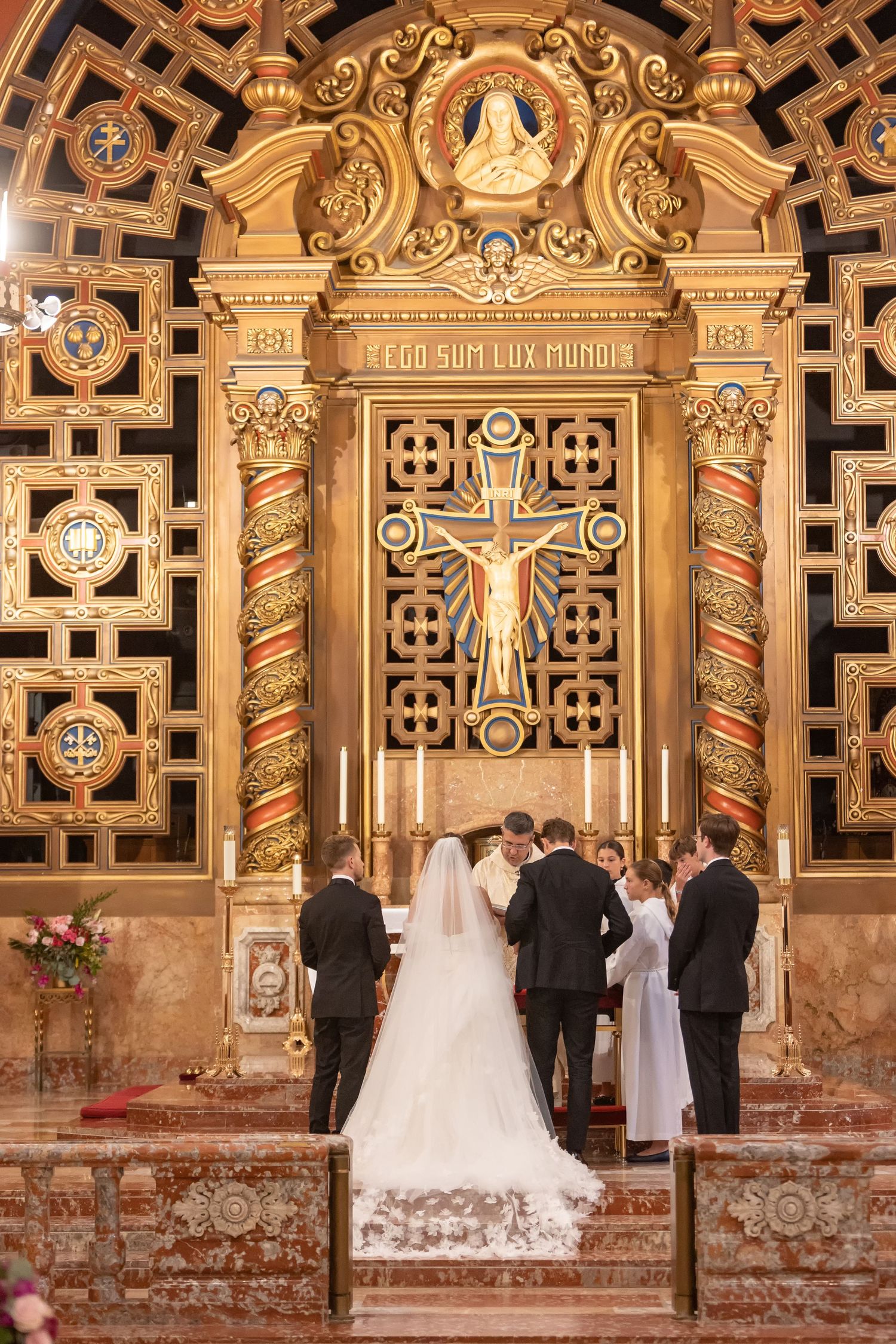 Bride and groom exchange vows at ornate golden altar with crucifix in elegant Catholic church wedding ceremony.