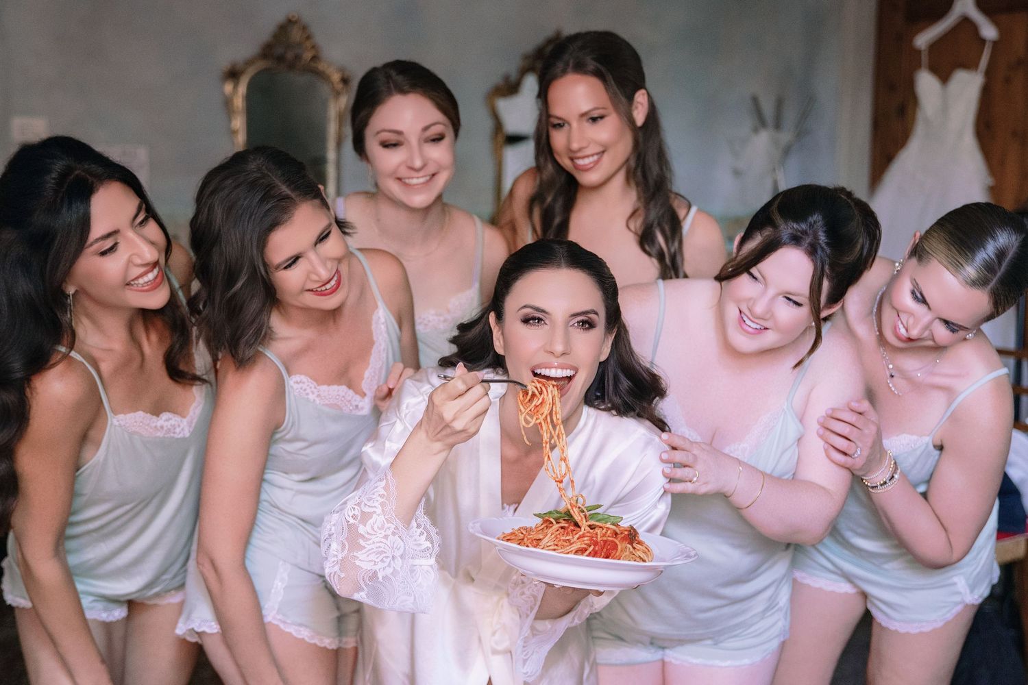 Bridesmaids in light colored dresses share laughs during wedding celebrations.