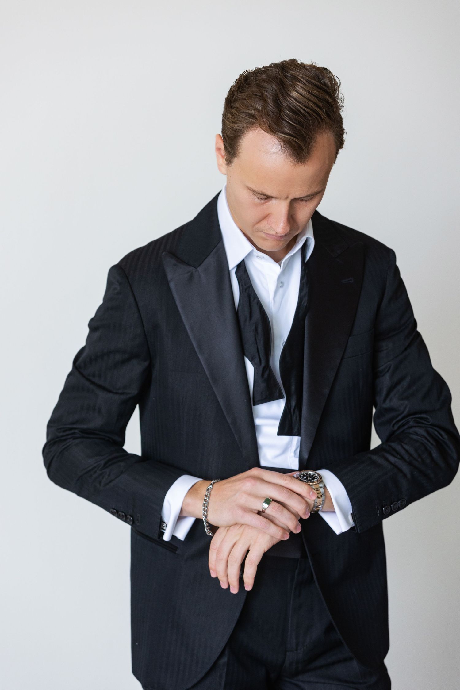Elegant man in black pinstripe tuxedo adjusting his cufflinks, wearing a watch and bracelet.