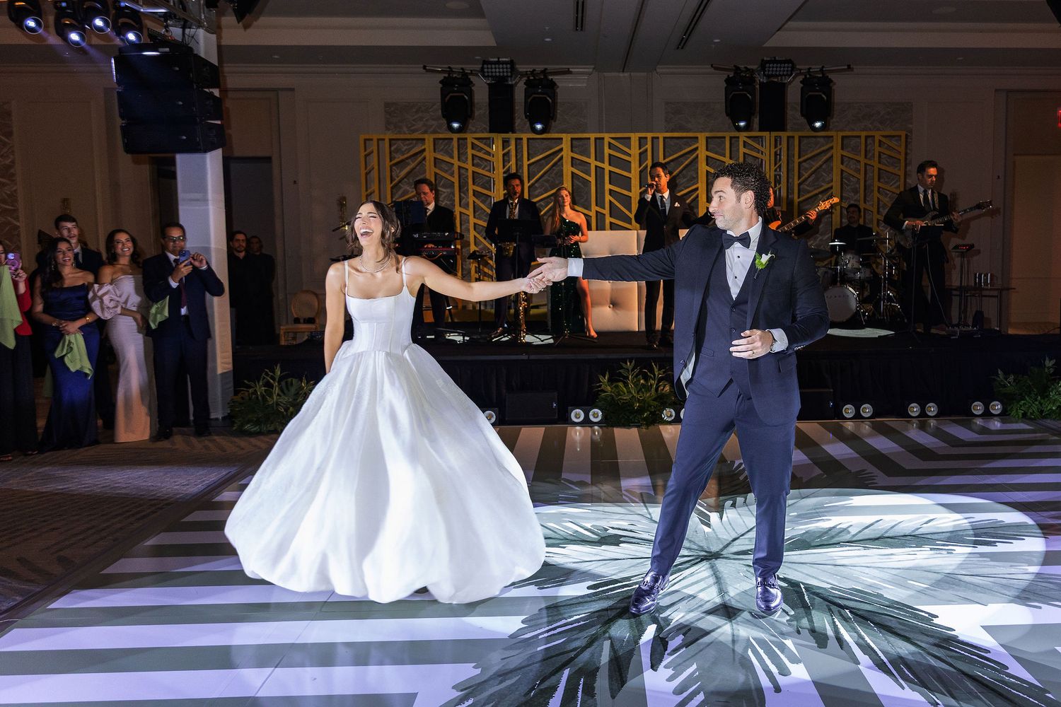A bride and groom share their first dance on an illuminated white dance floor at an elegant wedding reception.